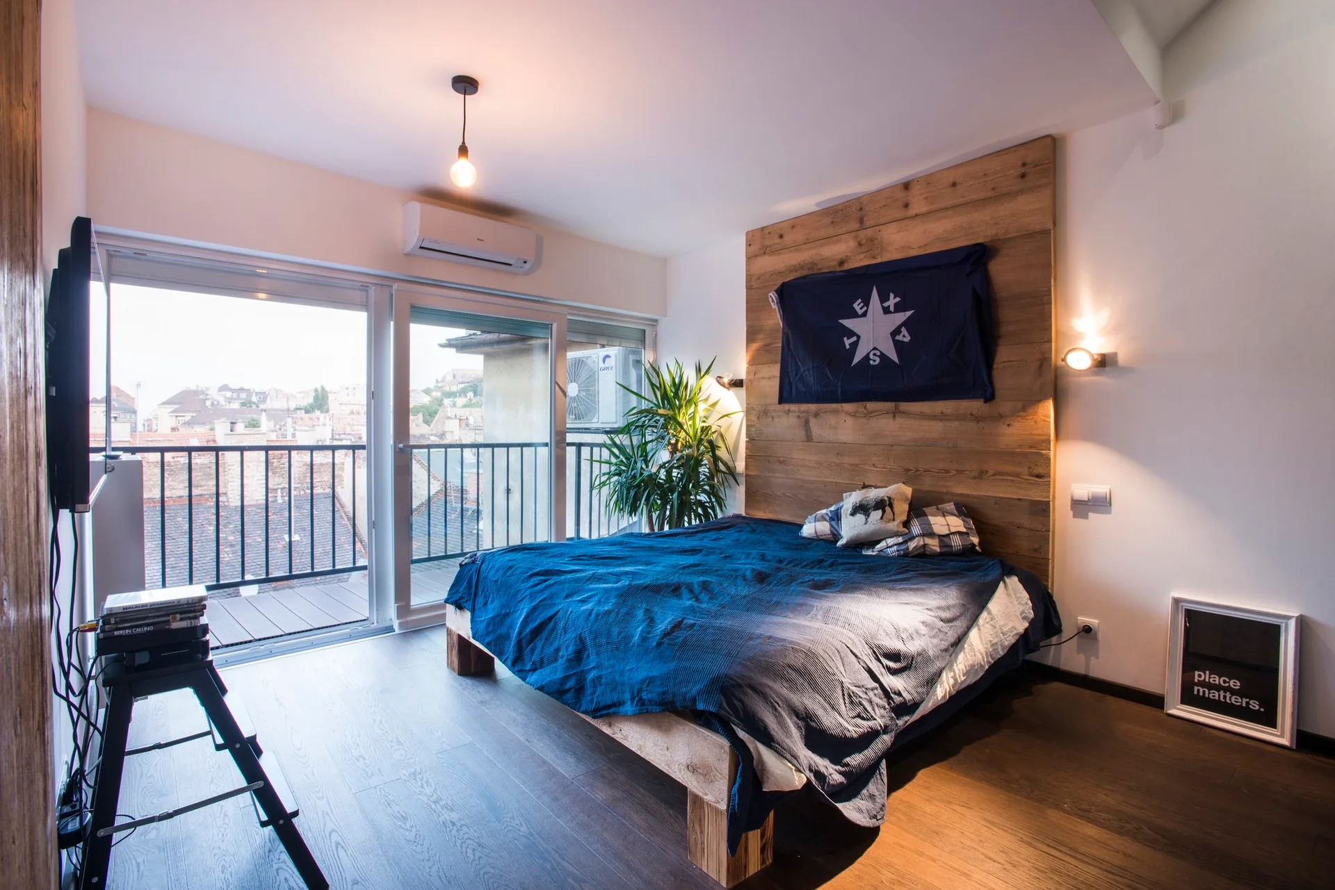 A bedroom features a platform bed with blue bedding, a vertical wood plank headboard, and sliding glass doors opening to a balcony.
