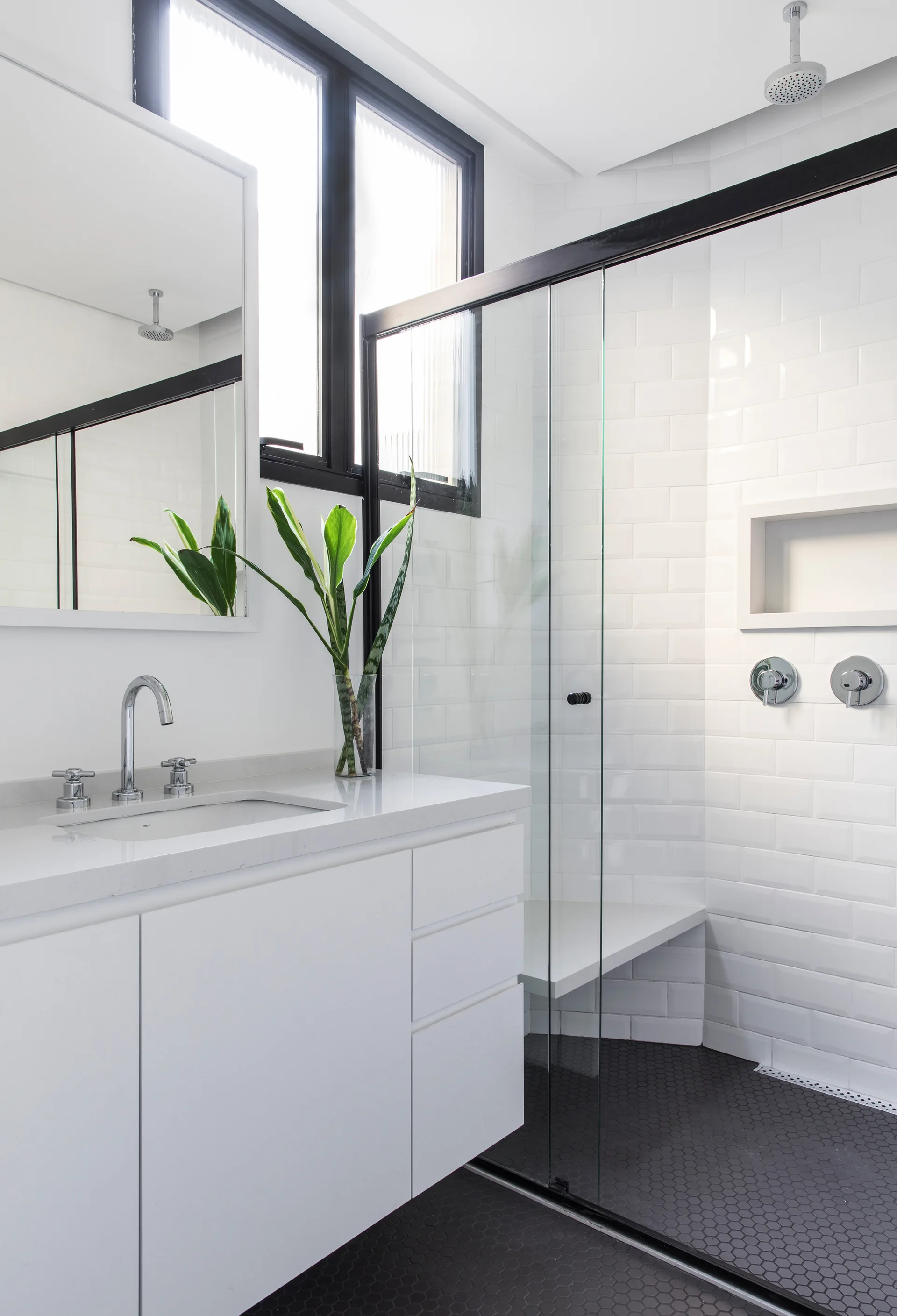 A modern bathroom features a white vanity, a glass shower with white subway tiles, and contrasting black hexagon floor tiles.