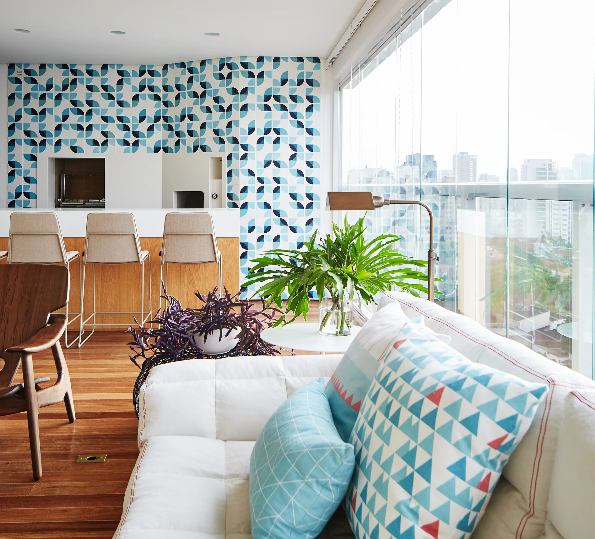A modern living area features a white sofa with patterned blue pillows, a wood-toned bar with stools, and a blue and white geometric wallpapered wall.