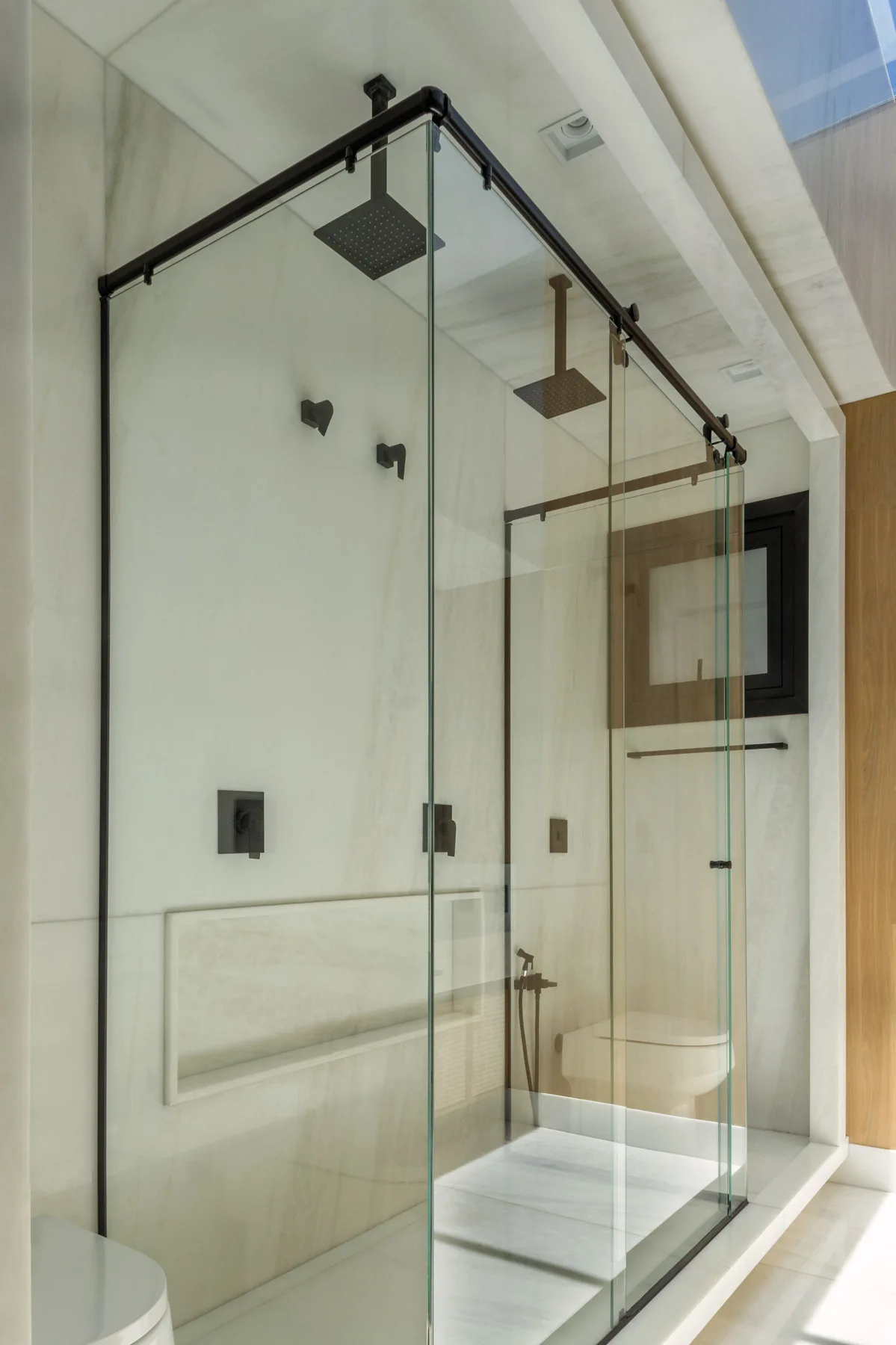A modern glass walk-in shower enclosure featuring large white marble walls and matte black rainfall showerheads.