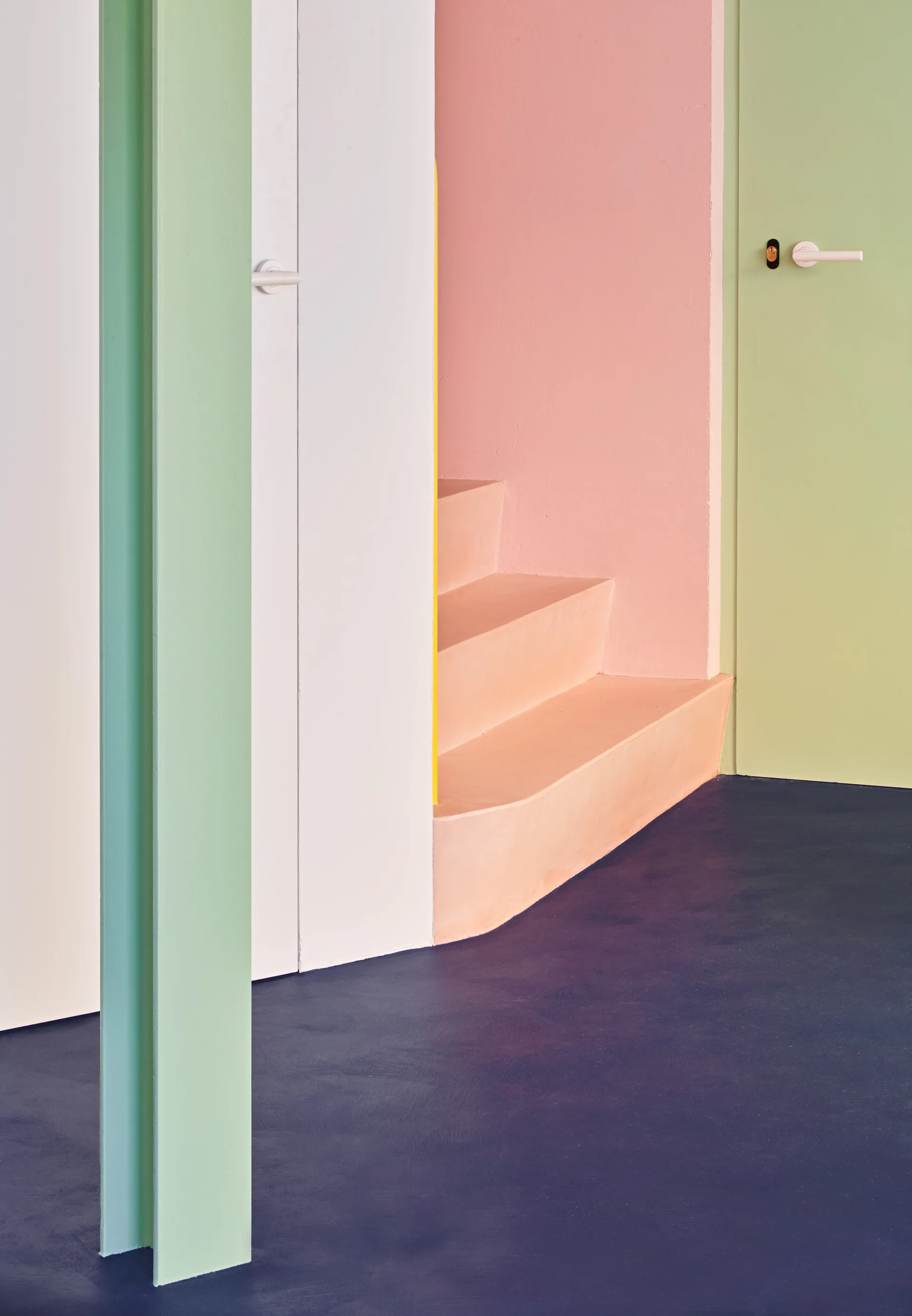 A minimalist interior features a peach-colored staircase, a light green door, and pink and white walls above a dark blue floor.