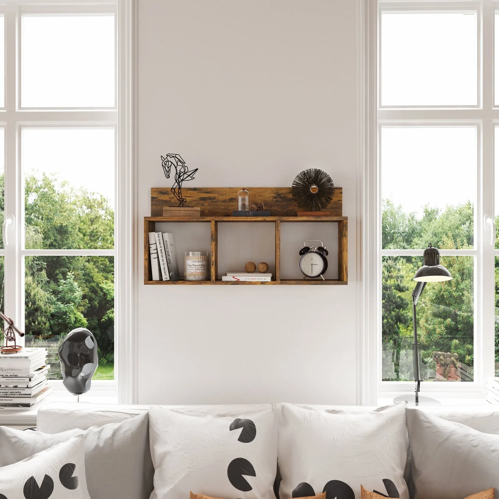 A rustic wooden wall shelf sits between two large windows above a white sofa with patterned pillows in a brightly lit room.