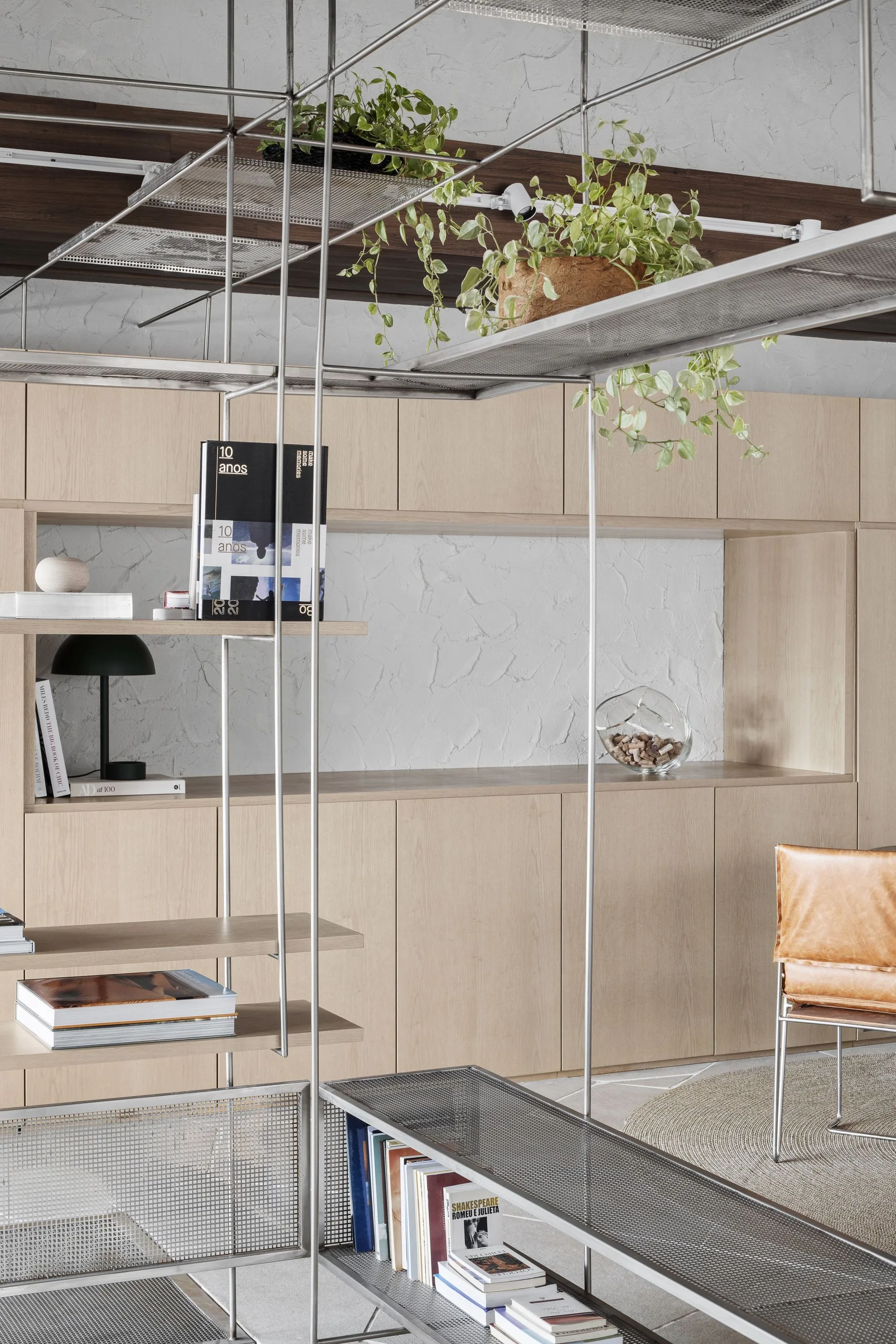 A modern metal grid shelving unit stands in front of flat-front light wood built-in cabinets on a textured plaster wall.
