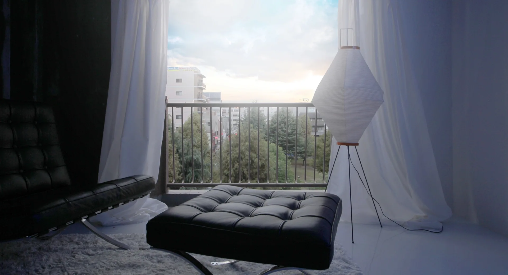 A modern lounge area with a black tufted leather chair and ottoman on a shag rug by a balcony window and paper floor lamp.