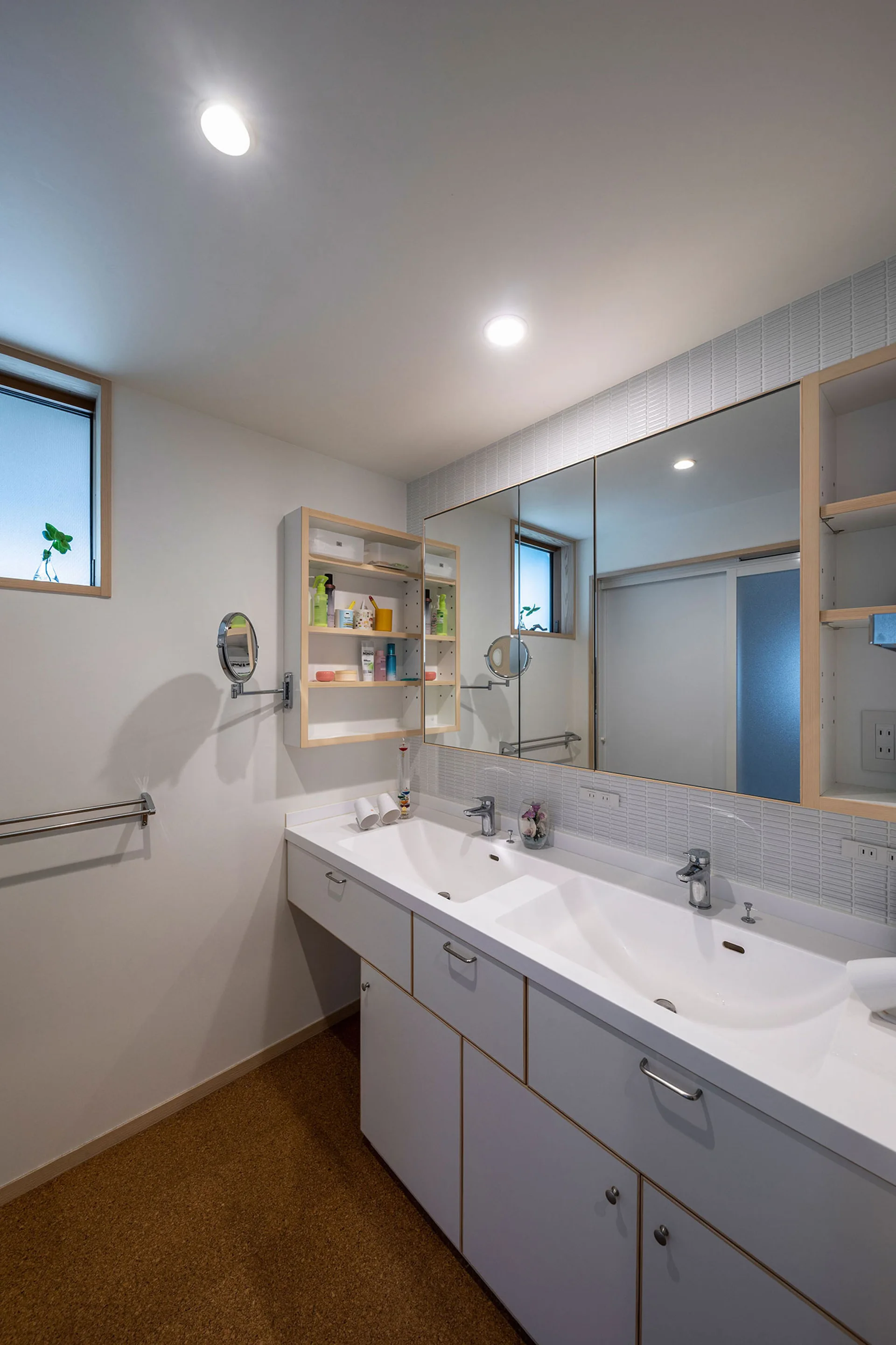 A modern bathroom features a double white vanity, wood-trimmed mirrored medicine cabinets, a linear tile backsplash, and textured cork flooring.