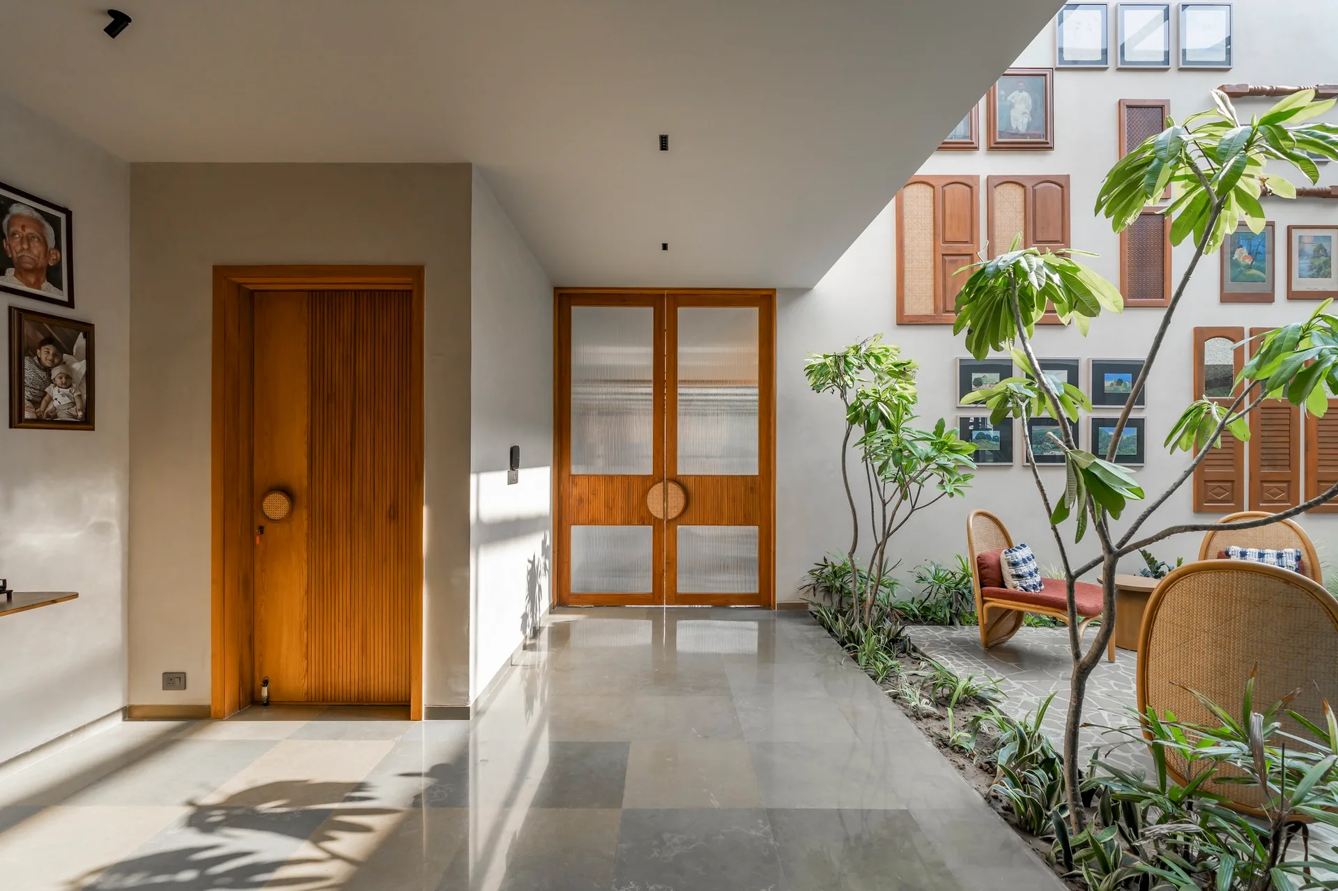 A tiled hallway leads to an indoor courtyard featuring a garden bed, rattan seating, and wooden doors with fluted glass panels.
