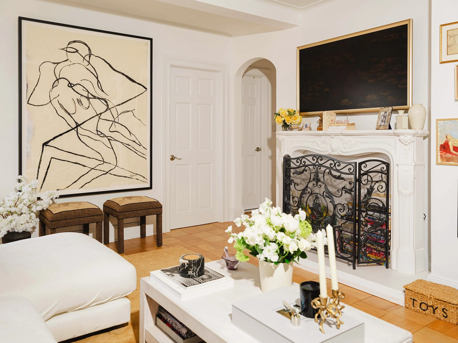 A bright living room featuring an ornate white fireplace, a framed television above the mantel, and large abstract line art on the wall.