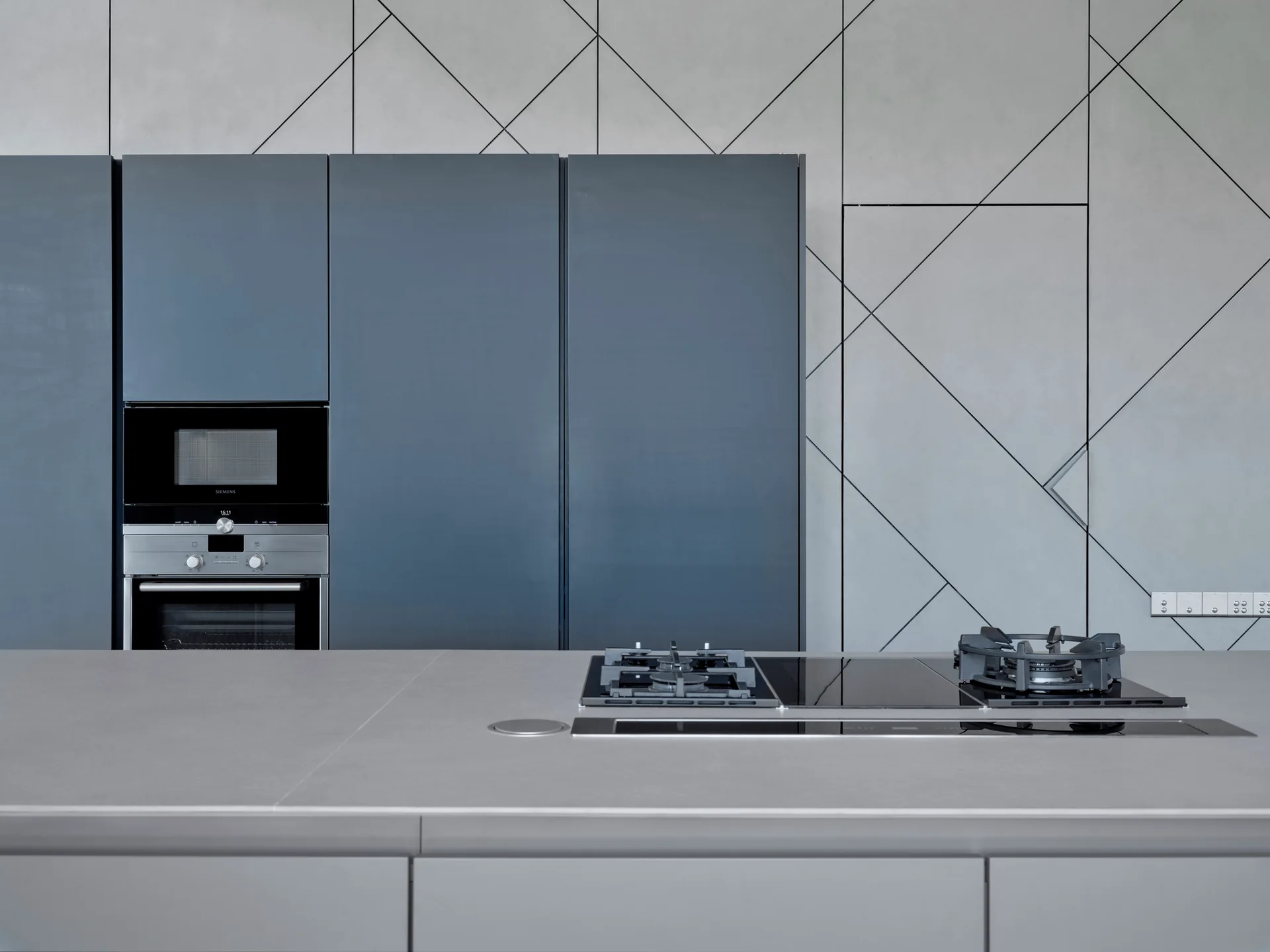 A minimalist kitchen features blue cabinetry with built-in appliances and a gray accent wall detailed with thin, black geometric lines.