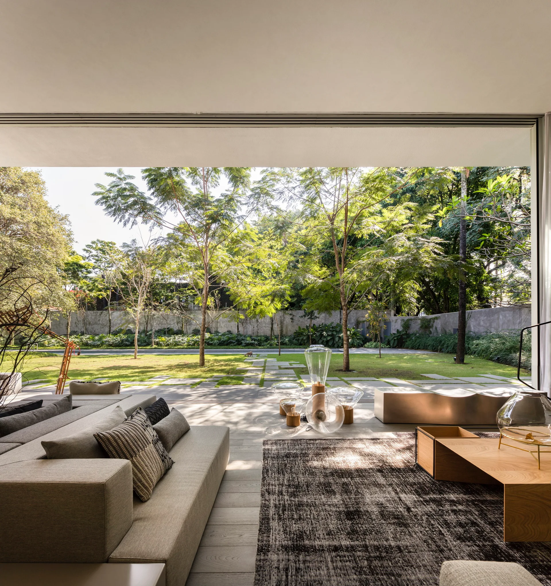 A low-profile grey sectional sofa and wooden coffee table sit in a living room that opens directly to a green backyard through wide sliding glass doors.
