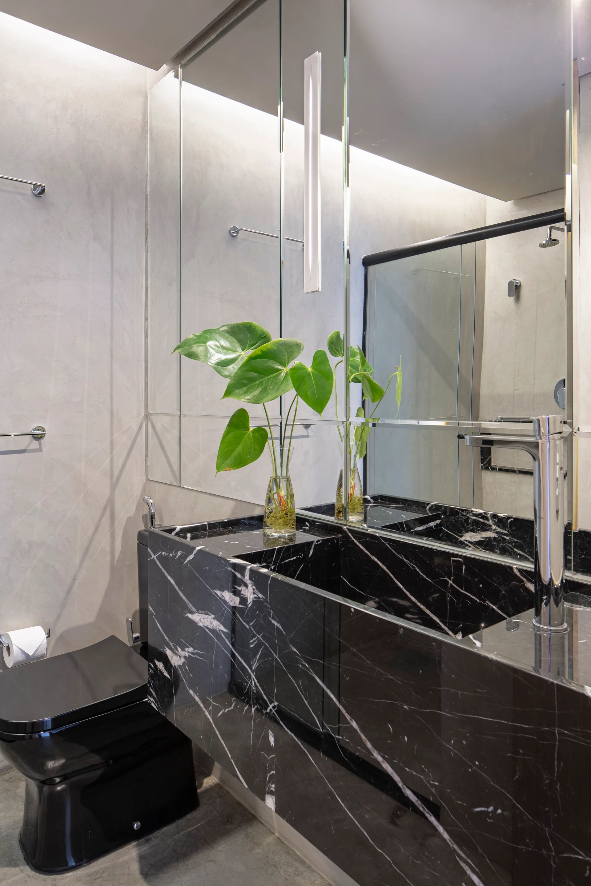 A modern bathroom features a black marble vanity with an integrated sink, a black toilet, gray textured walls, and large mirrored wall panels.