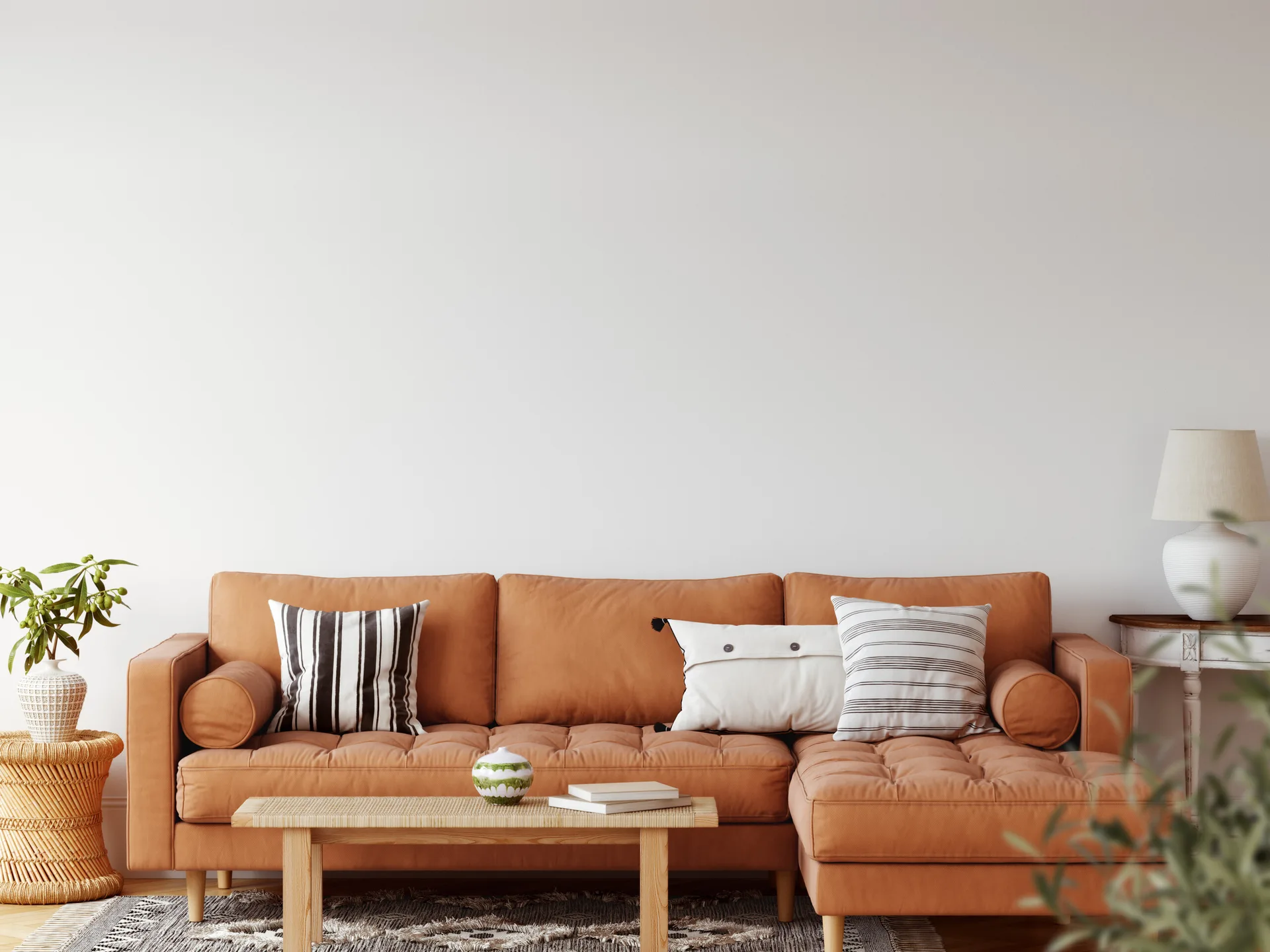 A terracotta tufted sectional sofa with striped pillows is positioned against a plain white wall next to a wooden coffee table and woven side table.