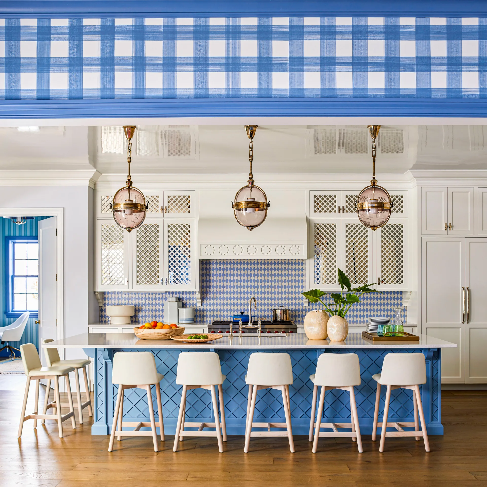 A blue and white kitchen features a blue lattice island with stools, diamond pattern tile backsplash, white cabinets, and plaid wallpaper.