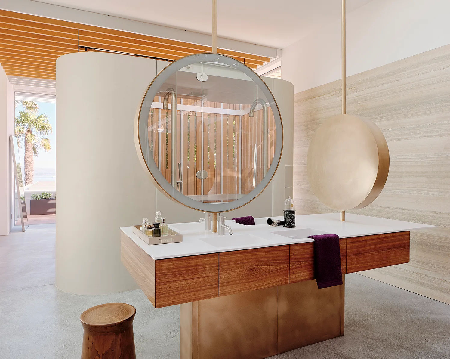 A modern bathroom features a wood vanity with a white countertop, two ceiling-suspended circular mirrors, and a curved partition wall.