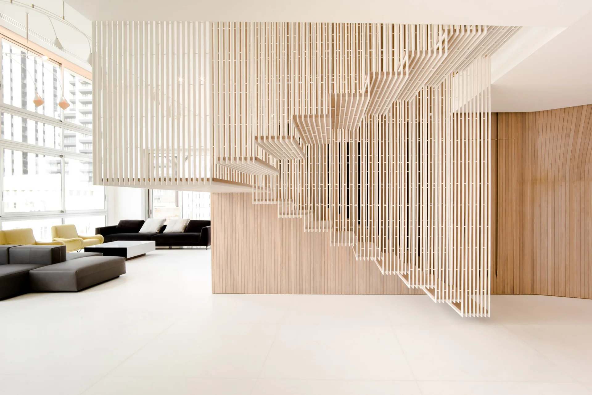 A modern living space featuring a dramatic white slatted wooden staircase structure suspended above a seamless white floor with minimalist furniture.
