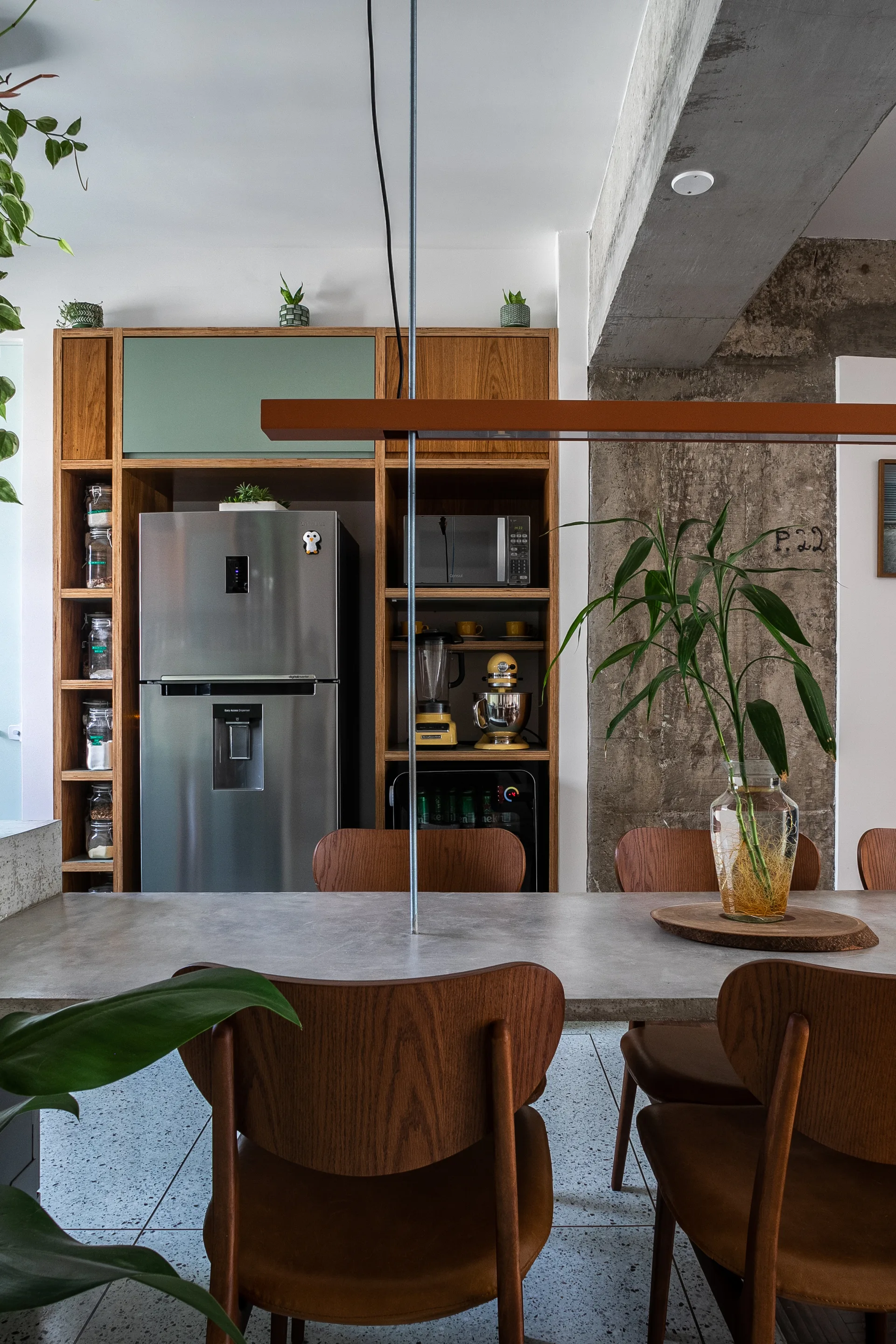 A dining table with wood chairs sits next to a large built-in wooden shelving unit holding a refrigerator, microwave, and mixers.
