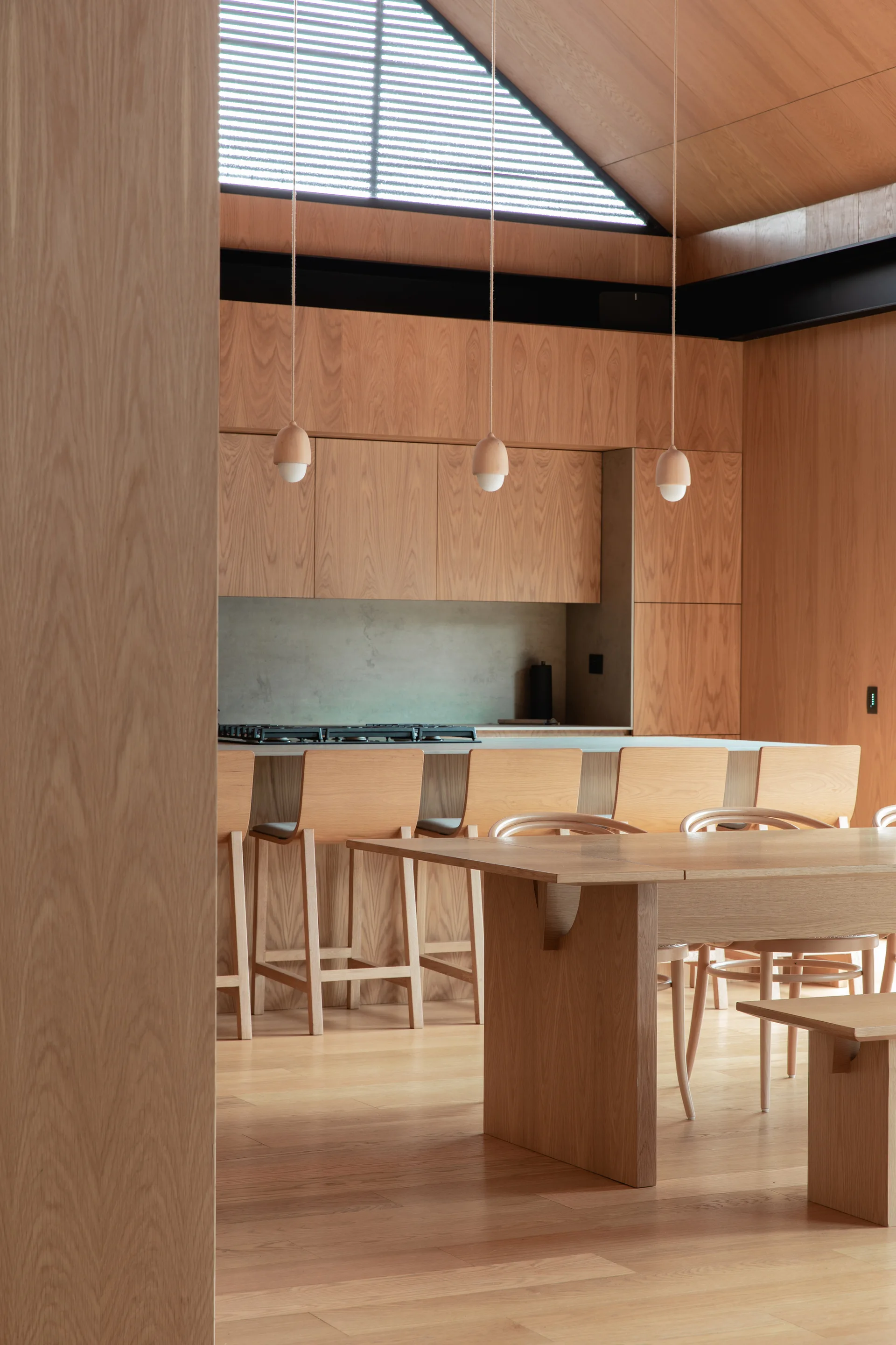 A wood-paneled kitchen features a matching island with stools, a dining table, suspended wooden pendant lights, and a vaulted ceiling with a skylight.