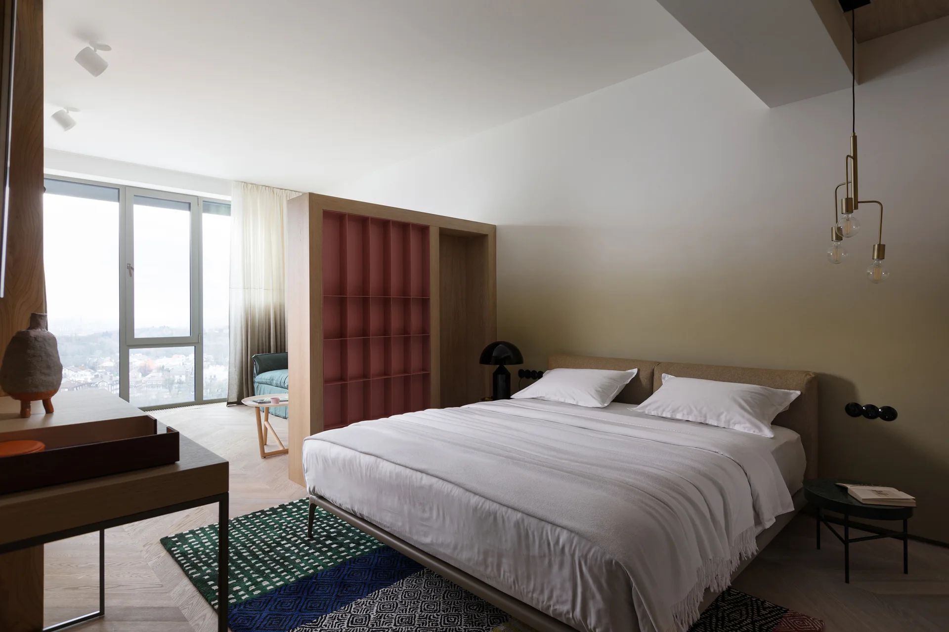 A modern bedroom features a bed with white linens, a wooden room divider with pink shelves, and a green ombre accent wall.