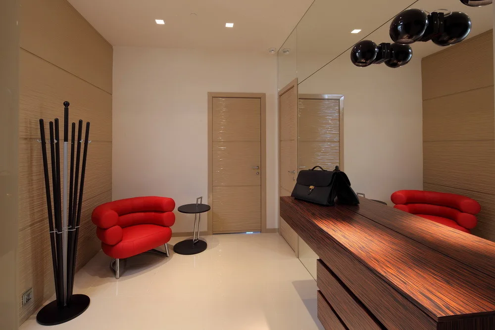 A modern entryway features a bright red curved armchair, a dark striped wood console table, and a large wall mirror.