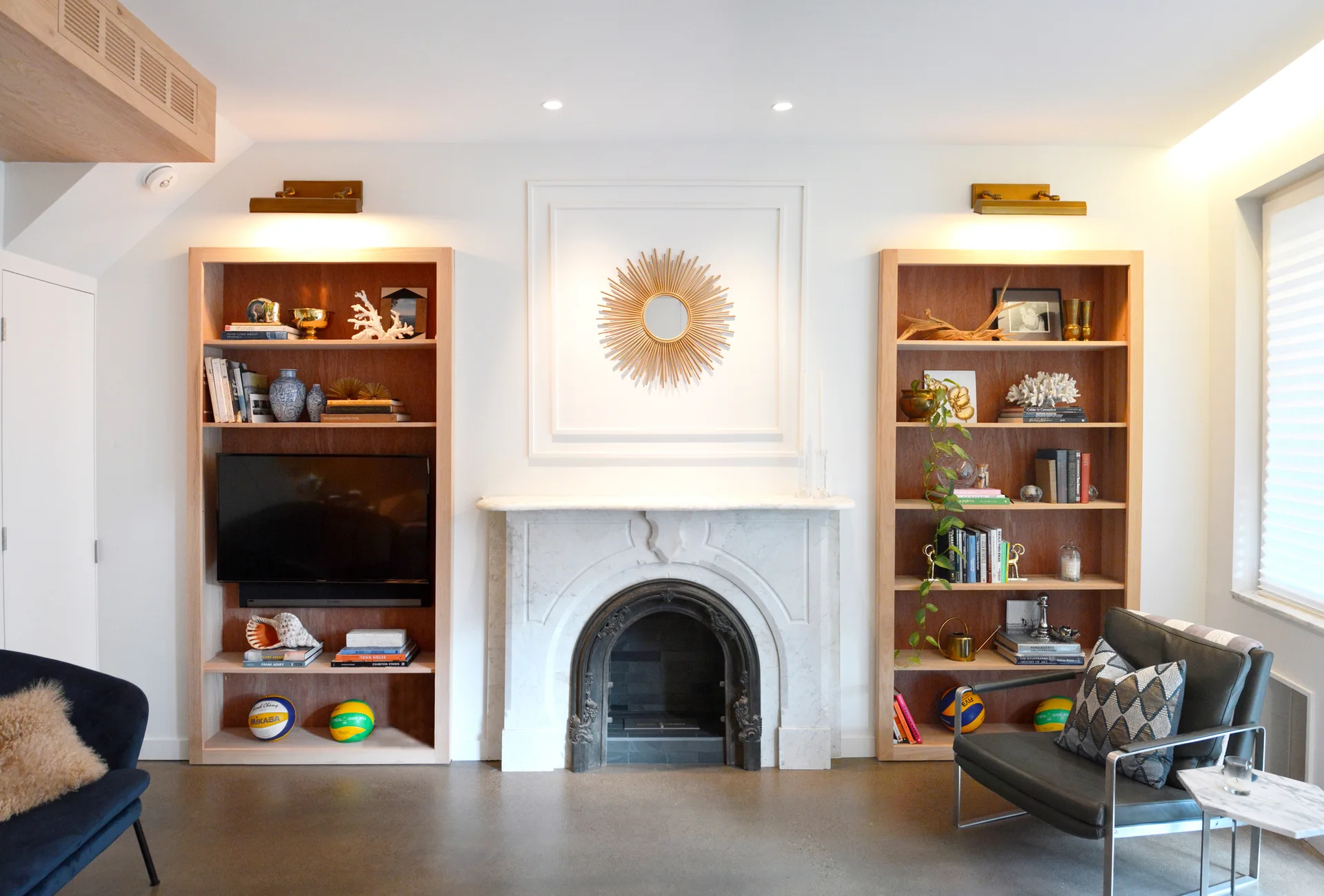 Symmetrical living room featuring an arched white marble fireplace flanked by tall light wood bookcases, topped with gold picture lights.