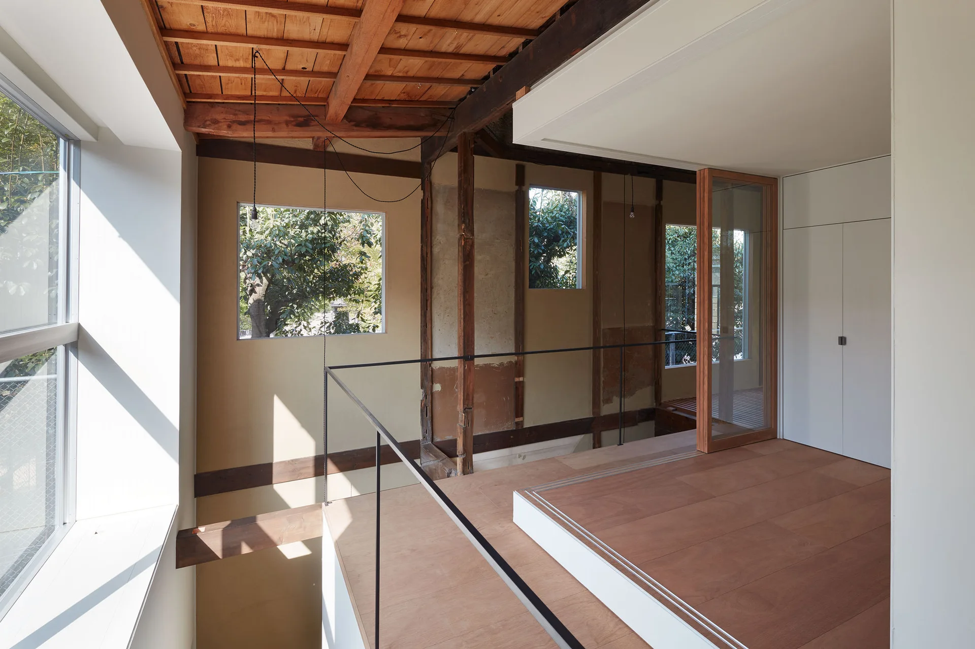 An elevated wood-plank landing with exposed ceiling beams, beige walls, a thin black metal railing, and white flat-panel storage.