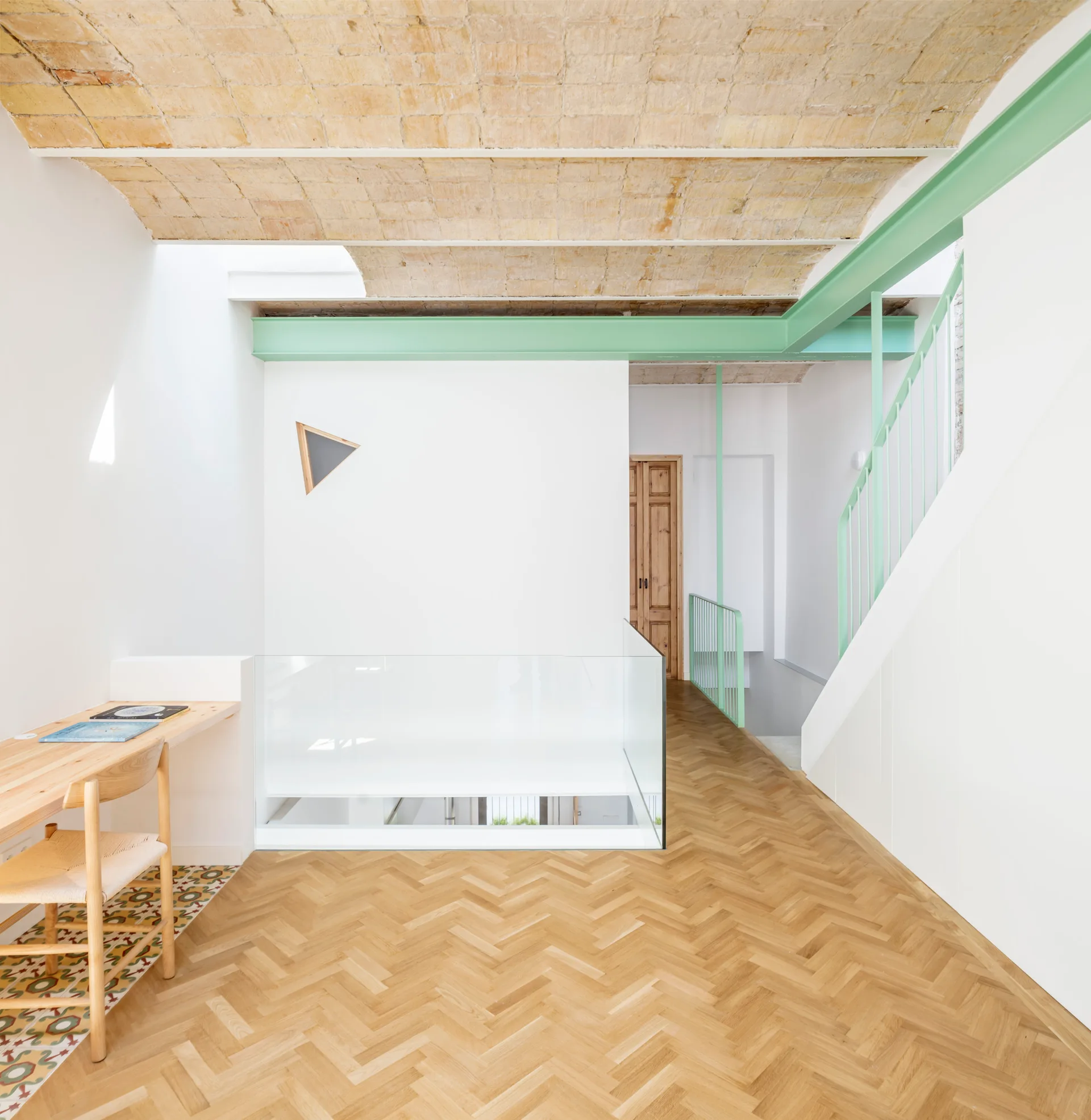 An open interior landing features a historic brick vaulted ceiling, herringbone wood floors, a desk, and staircase with a mint green railing.