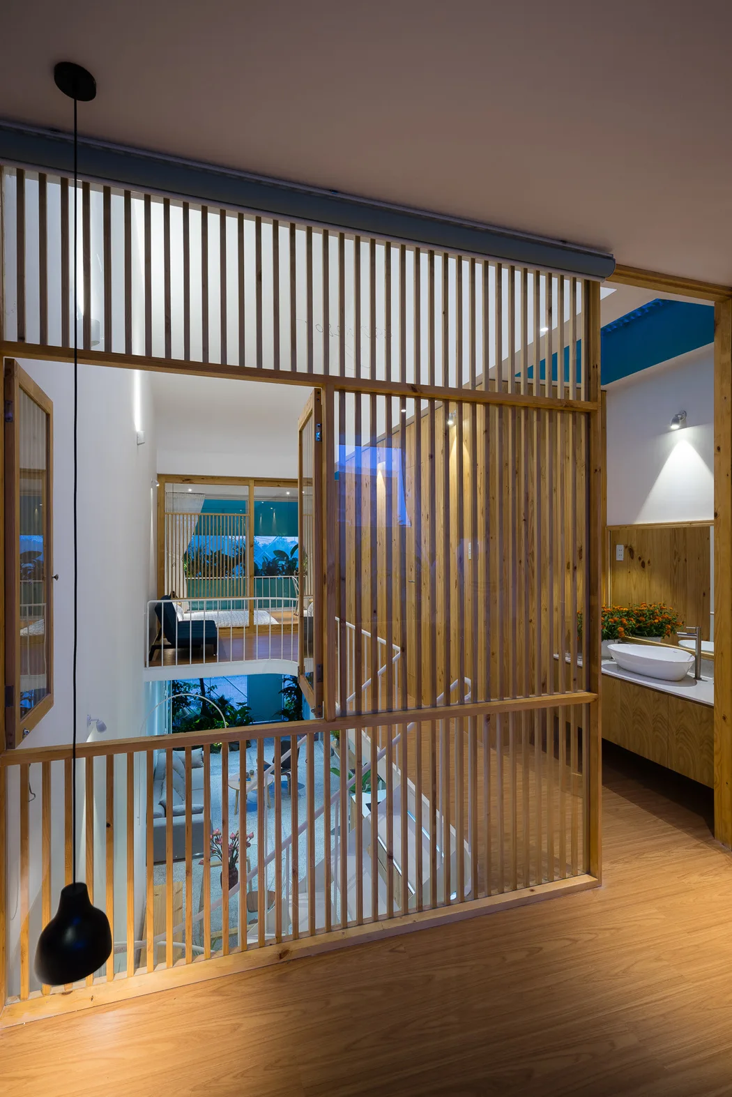A multi-level interior featuring a vertical slatted wood partition wall, a floating vanity with a white basin, and a staircase descending to a lower level.