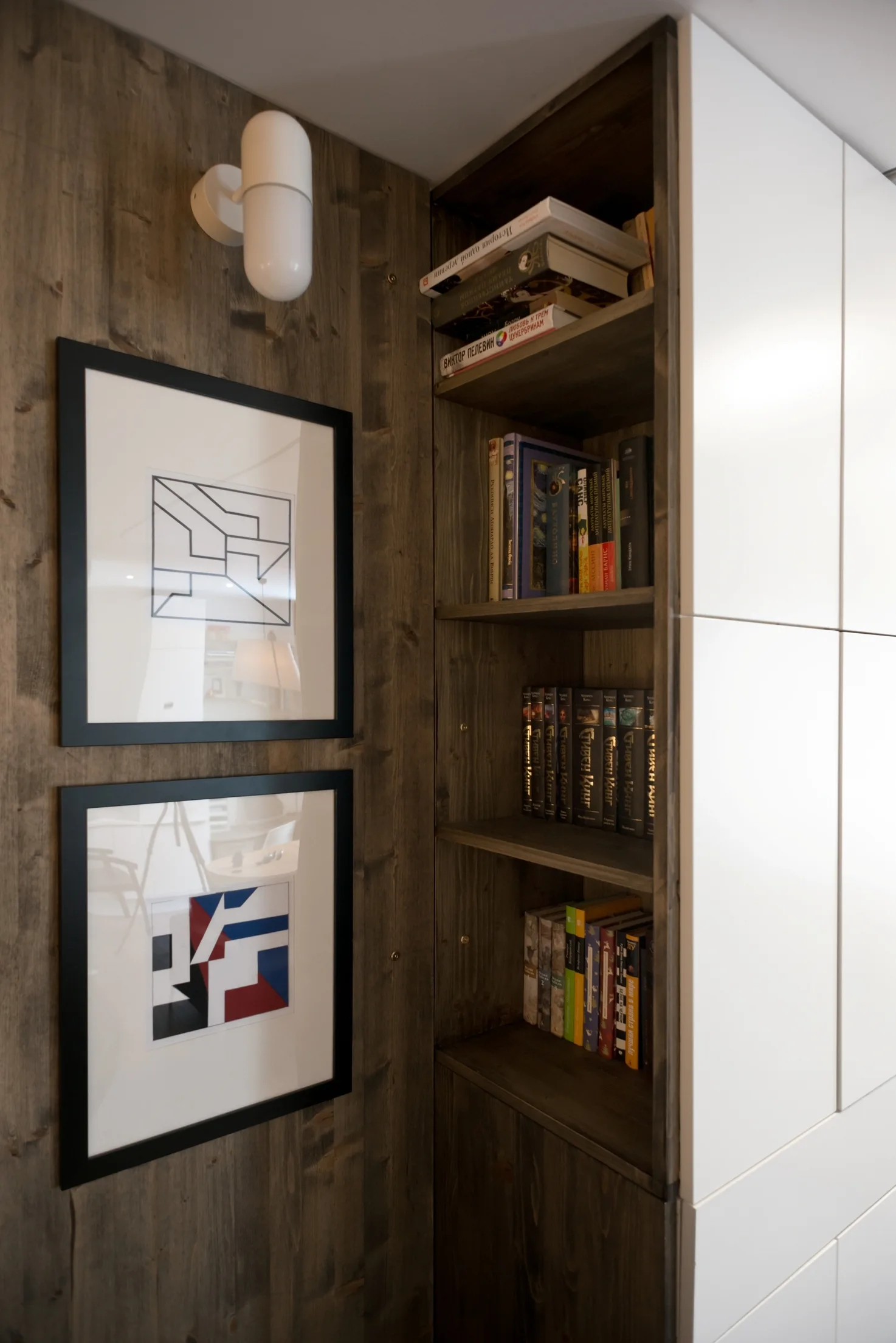 Built-in dark wood bookshelves set between a matching wood plank wall with framed art and modern white flat-panel cabinets.