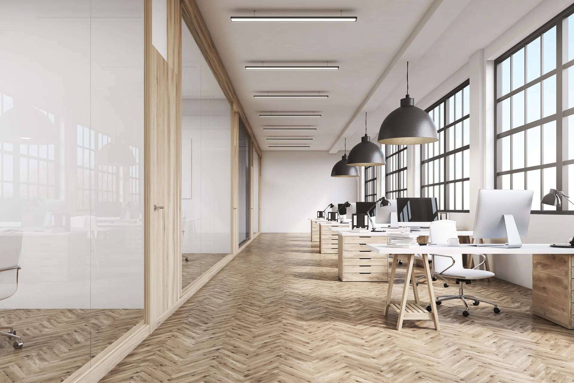 A modern open-plan office workspace featuring white desks, black pendant lights, herringbone wood floors, and floor-to-ceiling glass partitions.