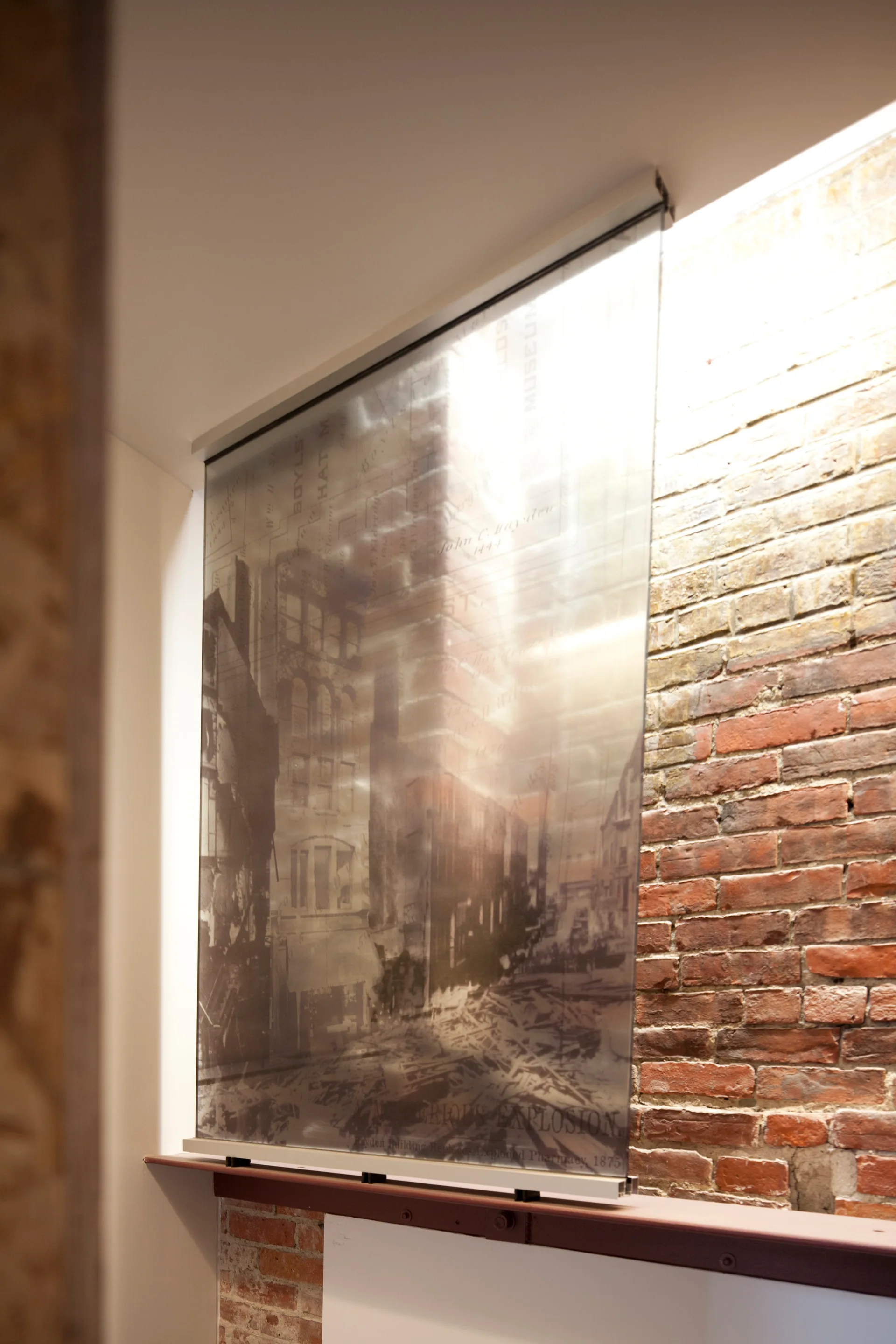 A semi-transparent historical graphic panel is mounted on a textured red brick wall under directional ceiling lighting.