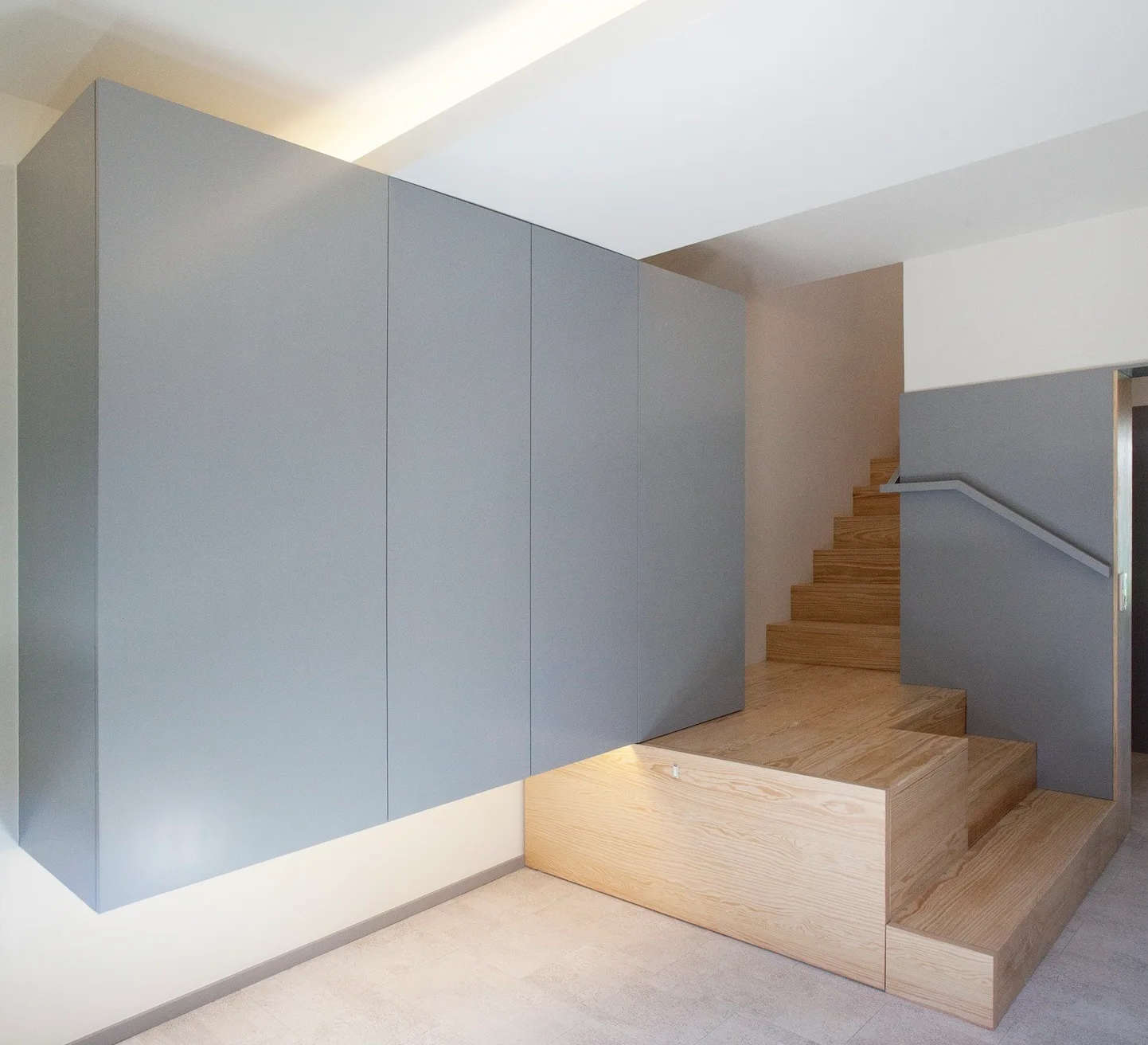 A minimalist wooden staircase features a large wall-mounted gray cabinet unit with indirect lighting glowing underneath.