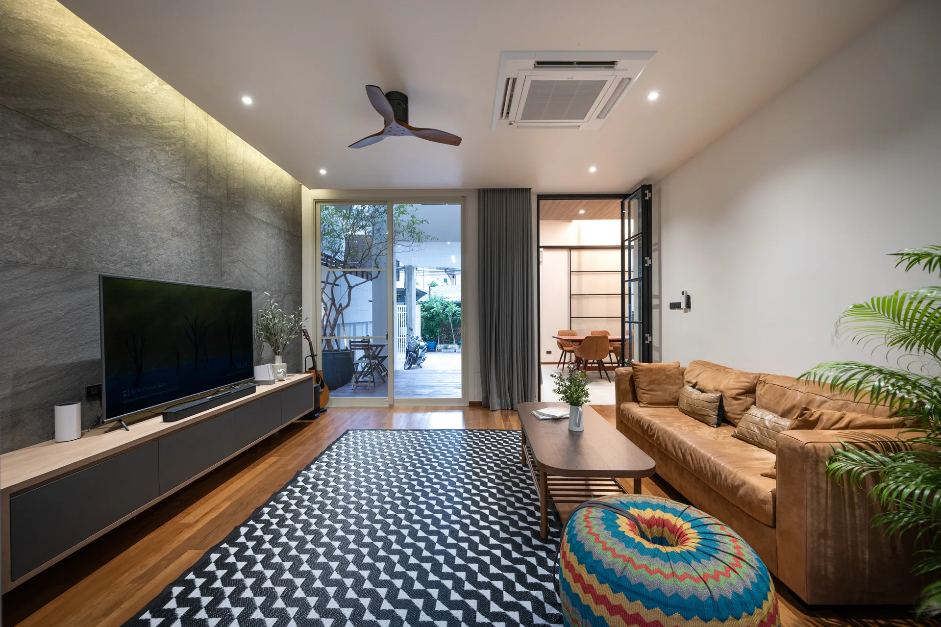 A modern living room features a brown leather sofa, a textured grey stone accent wall, and a black and white geometric area rug.