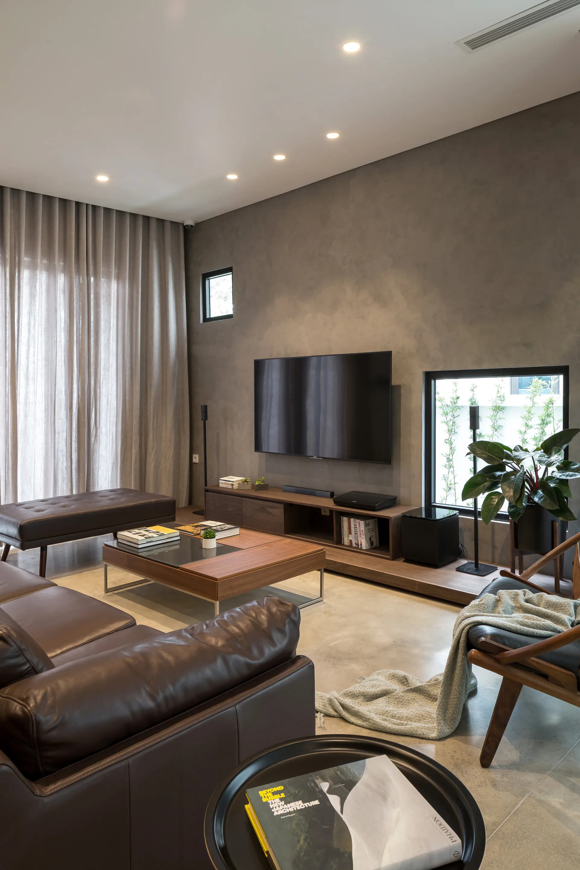 A contemporary living room featuring a textured grey feature wall behind a wall-mounted TV, a brown leather sofa, and a low wooden media console.