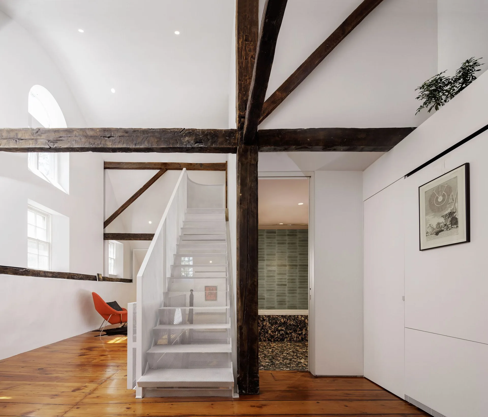 A white perforated metal staircase stands next to dark exposed timber beams on a light pine wood floor in a vaulted room.