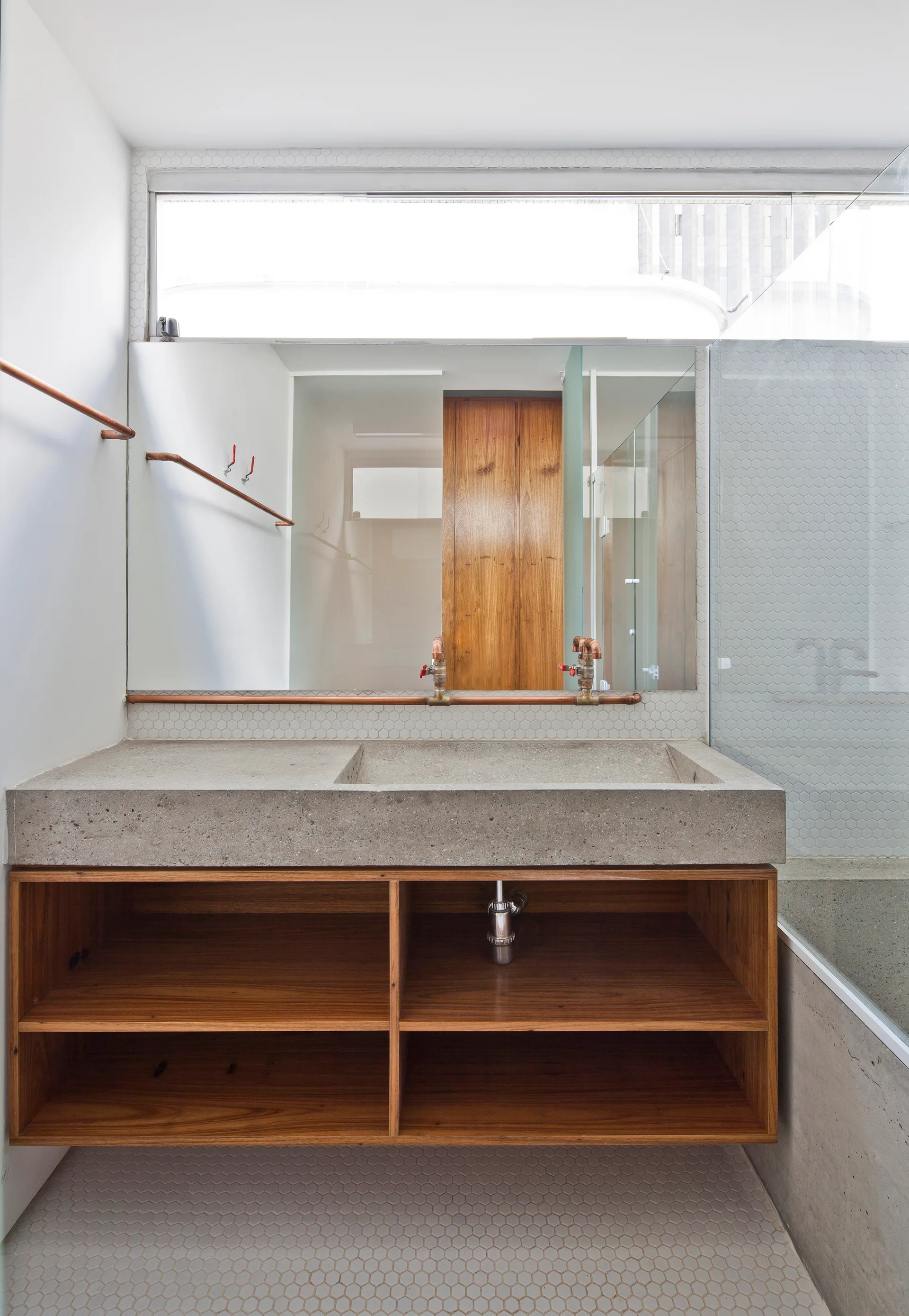 A minimalist bathroom vanity with a concrete sink, natural wood shelving, a large mirror, and exposed copper pipes.