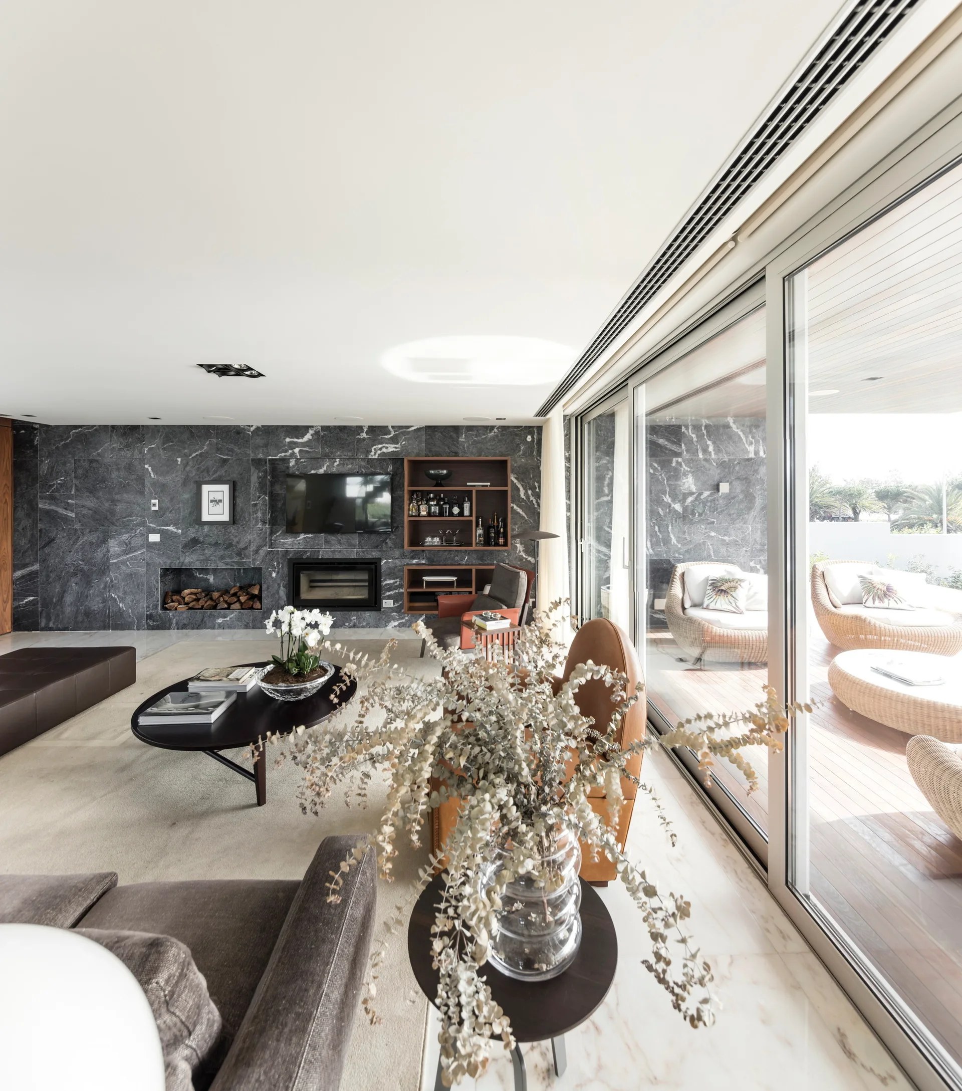 A modern living room featuring a dark gray veined stone fireplace wall and sliding glass doors that open to an outdoor patio with wicker furniture.