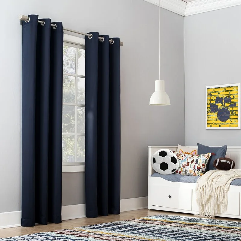 A kids bedroom features a white storage daybed with sports-themed pillows, a striped rug, and dark navy blue grommet curtains over a window.