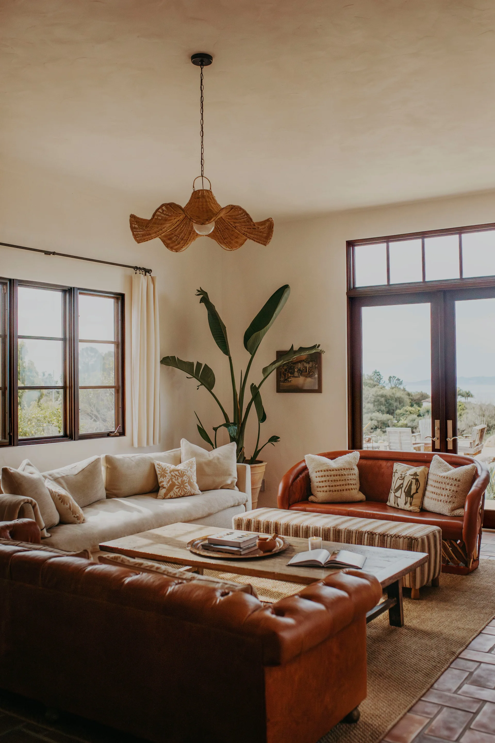 A warm living room features leather and cream sofas surrounding a low wood coffee table, anchored by a wavy woven pendant light.
