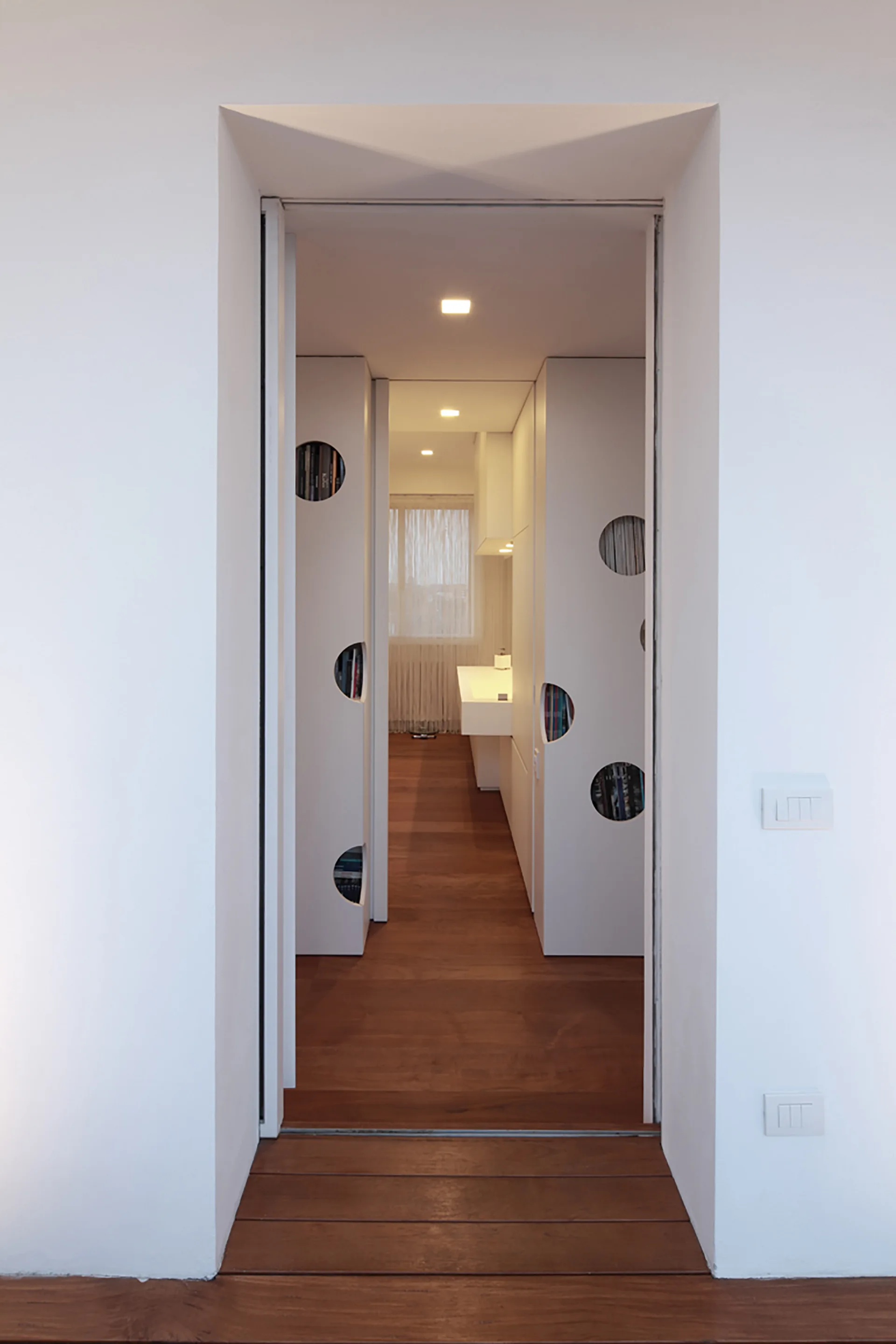A doorway looking into a hallway with dark wood floors and floor-to-ceiling white cabinets featuring large circular cutouts.