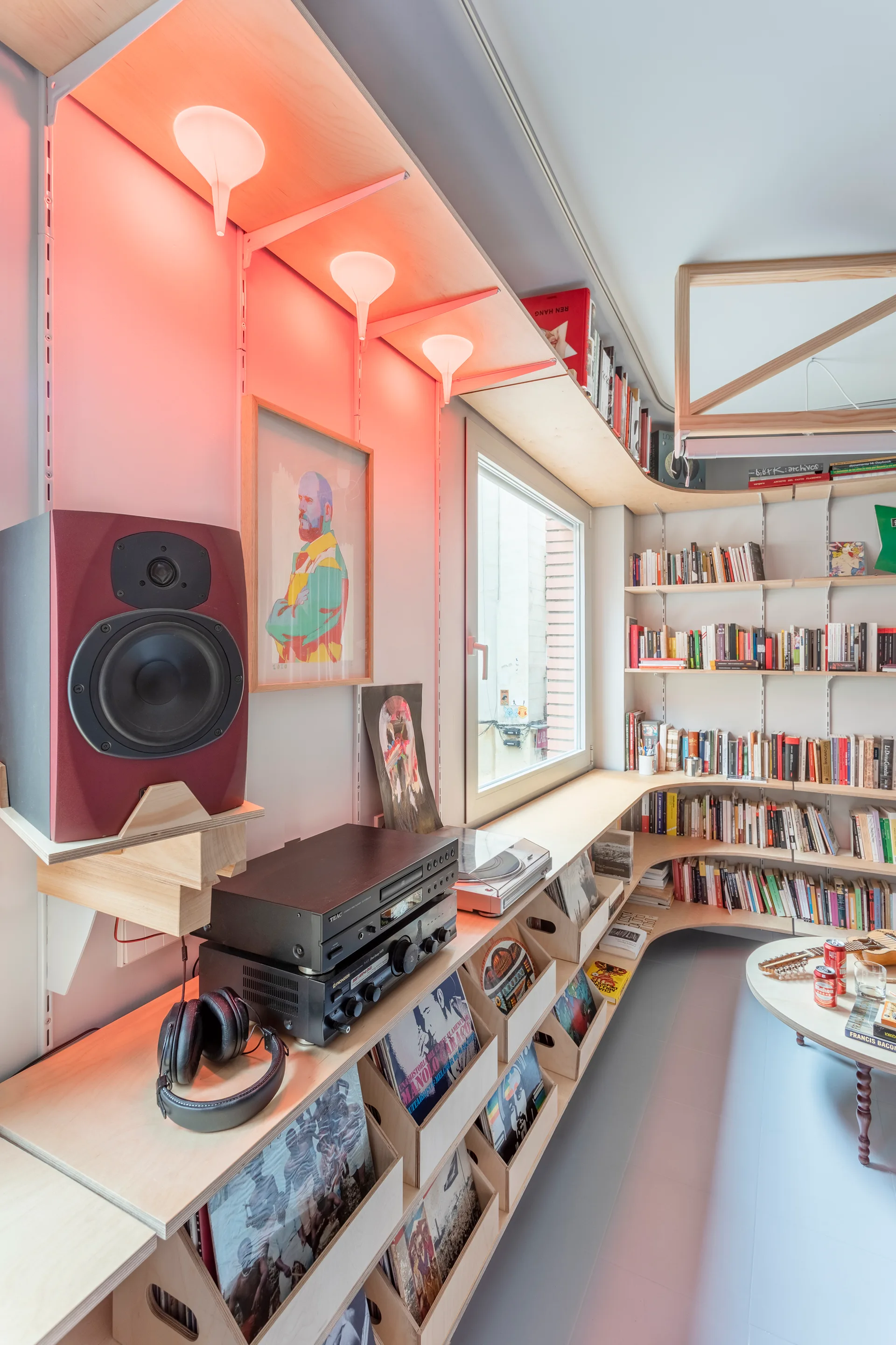 A modern library room featuring curved light wood bookshelves wrapped along a wall, complete with record player equipment and glowing orange lights.