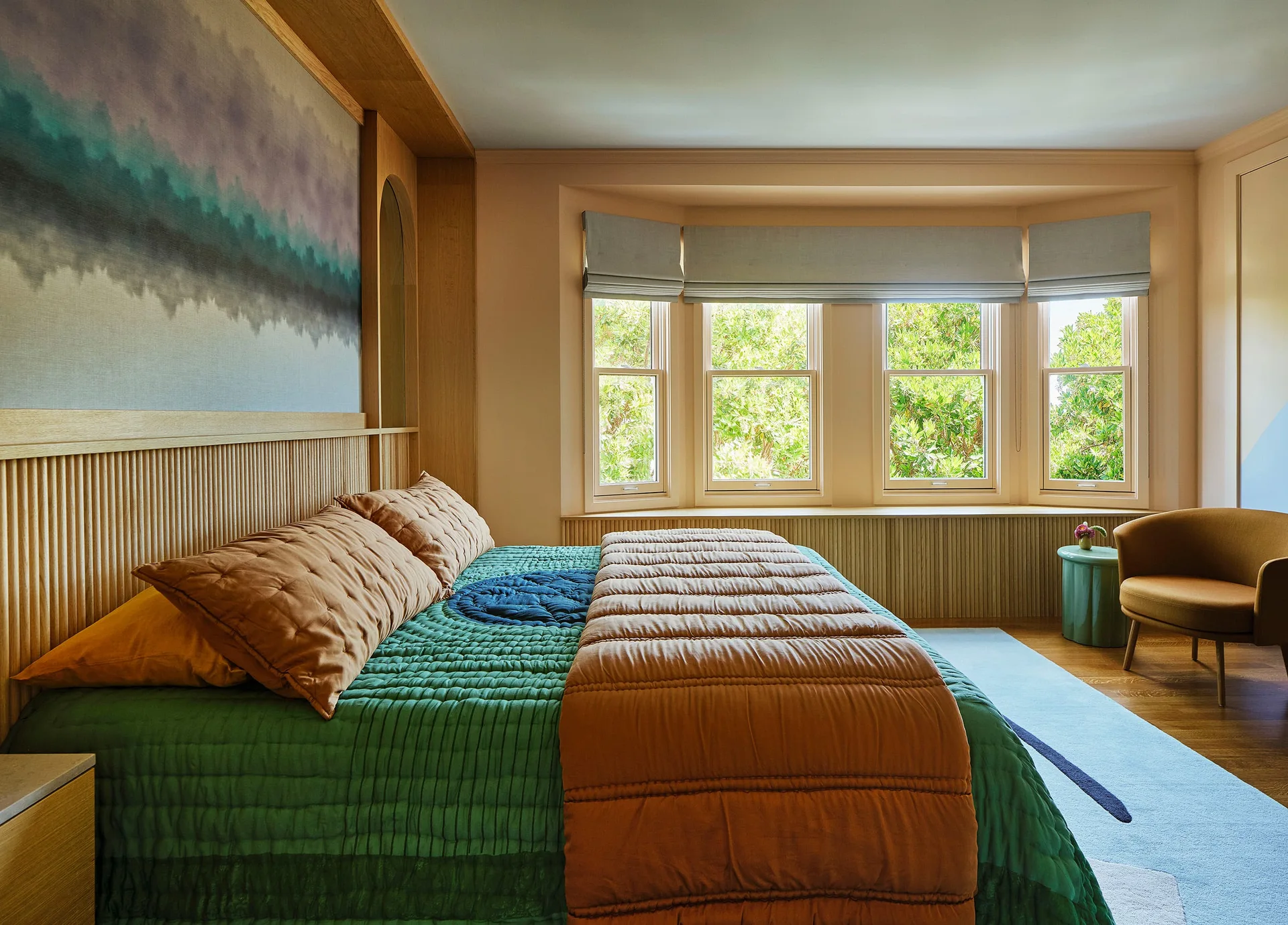 A bedroom featuring a bed with green and brown quilted bedding against a slatted wood headboard next to a bay window with a built-in ledge.