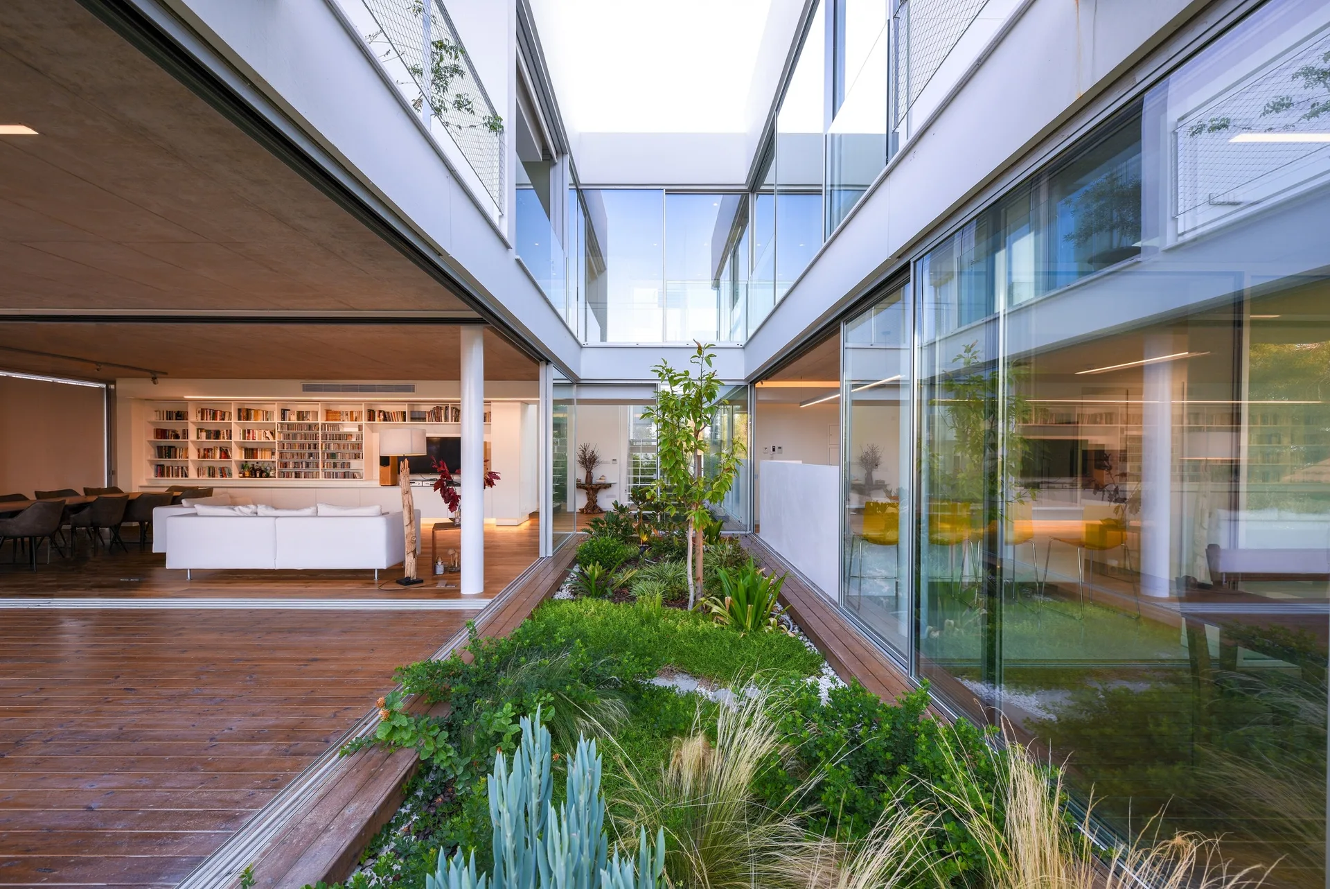 A modern home features glass-walled living spaces enclosing a central outdoor courtyard garden with lush plantings and wood decking.