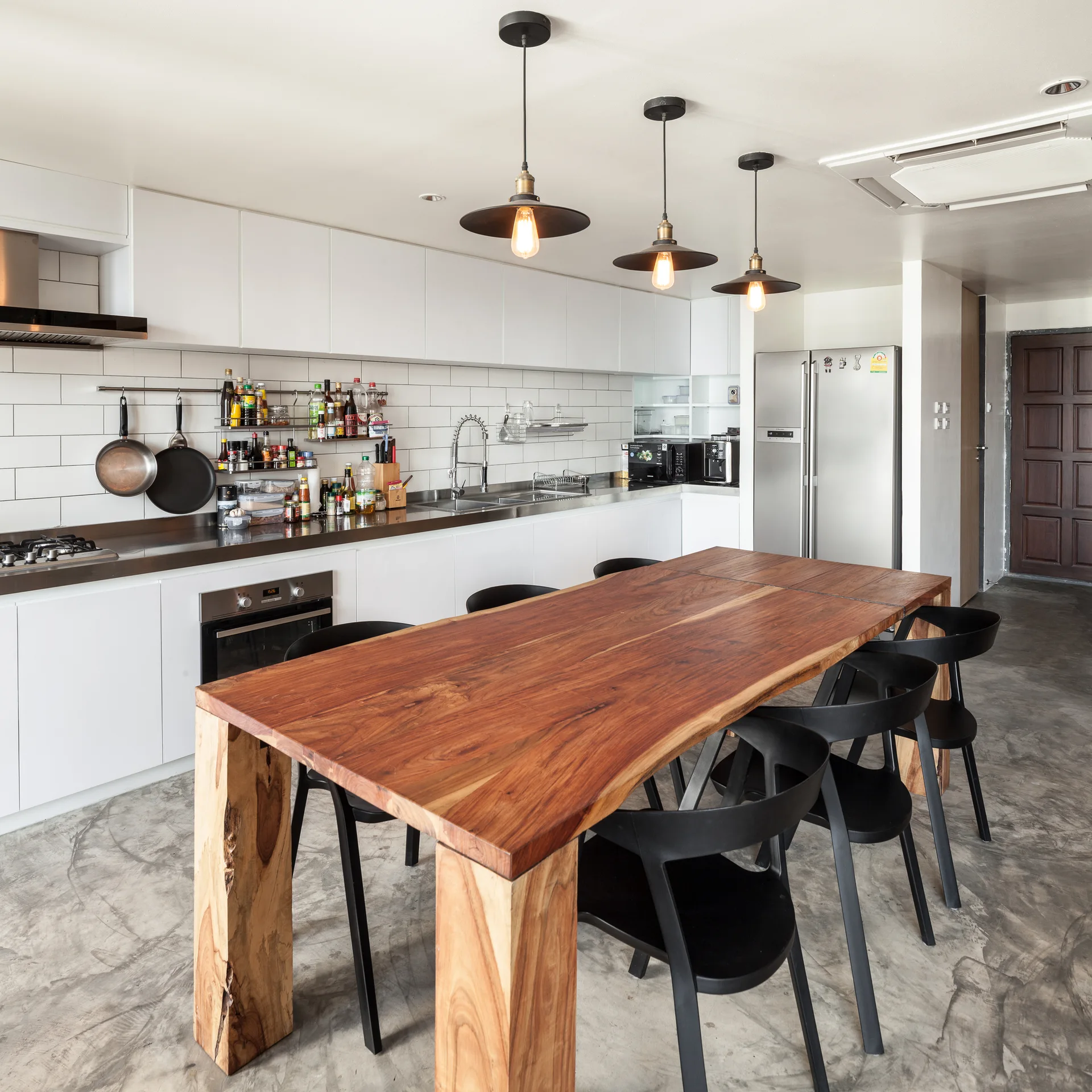 A modern industrial kitchen features white cabinetry, a large live-edge wood dining table with black chairs, and a polished concrete floor.