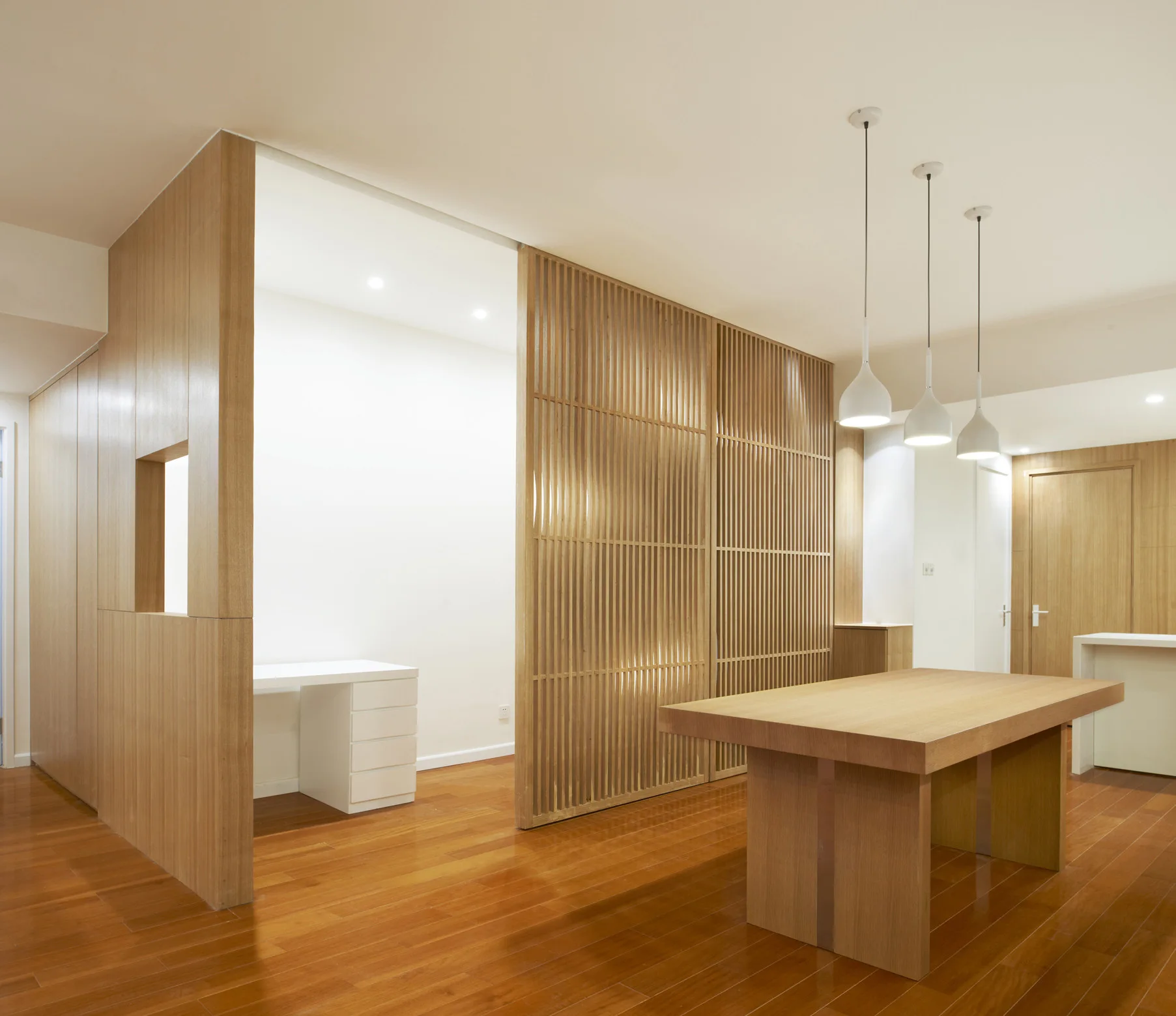 A modern room features a slatted wooden partition screen separating a wooden table from a home office desk.