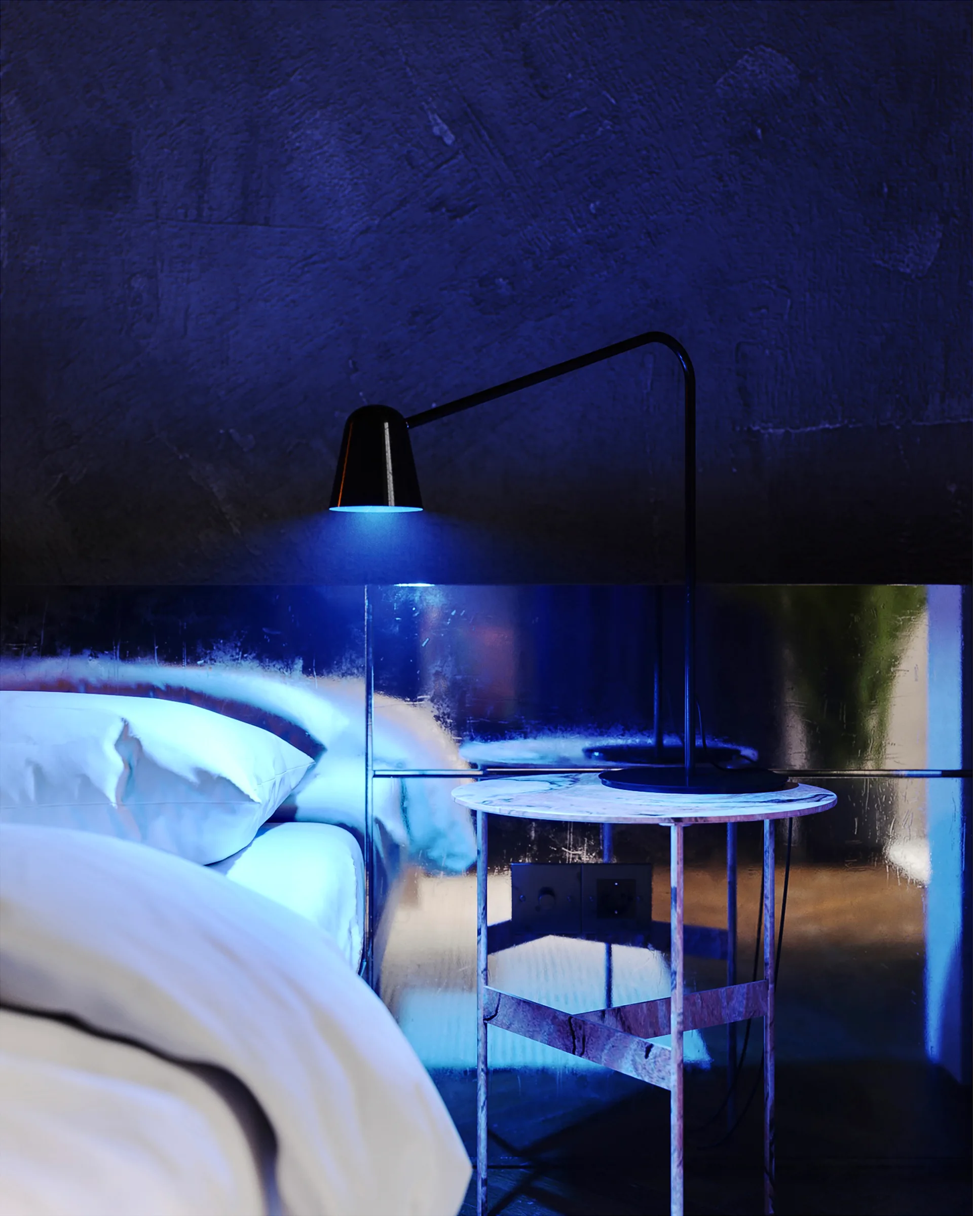 A marble bedside table with a black modern lamp sits next to a bed with white sheets under a blue spotlight reflection.