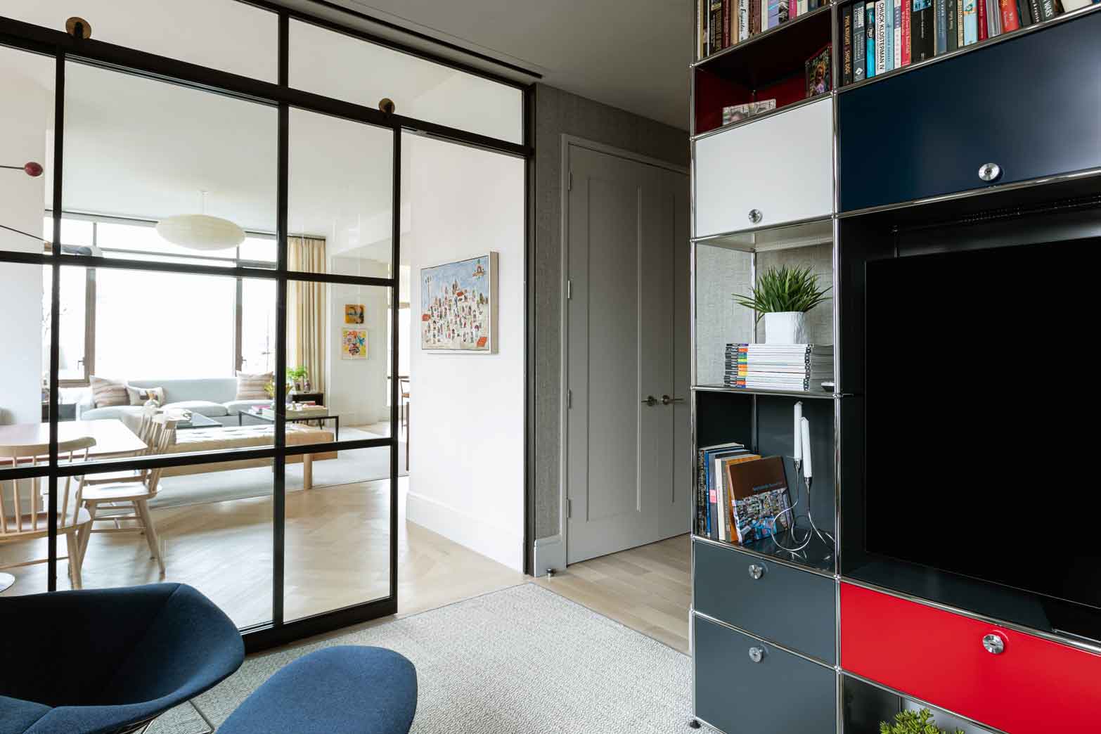 A modern home interior features a black metal framed glass partition separating a living room from a space with a colorful modular storage unit.