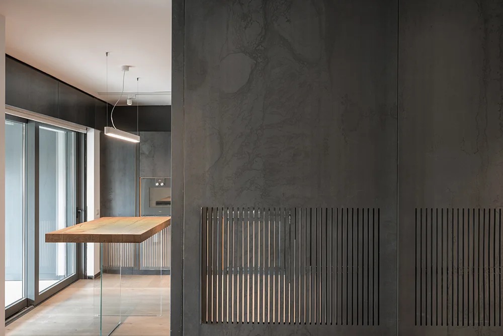 A modern kitchen featuring dark stone-like wall panels with vertical slatted vents and a floating wooden island on clear glass legs.