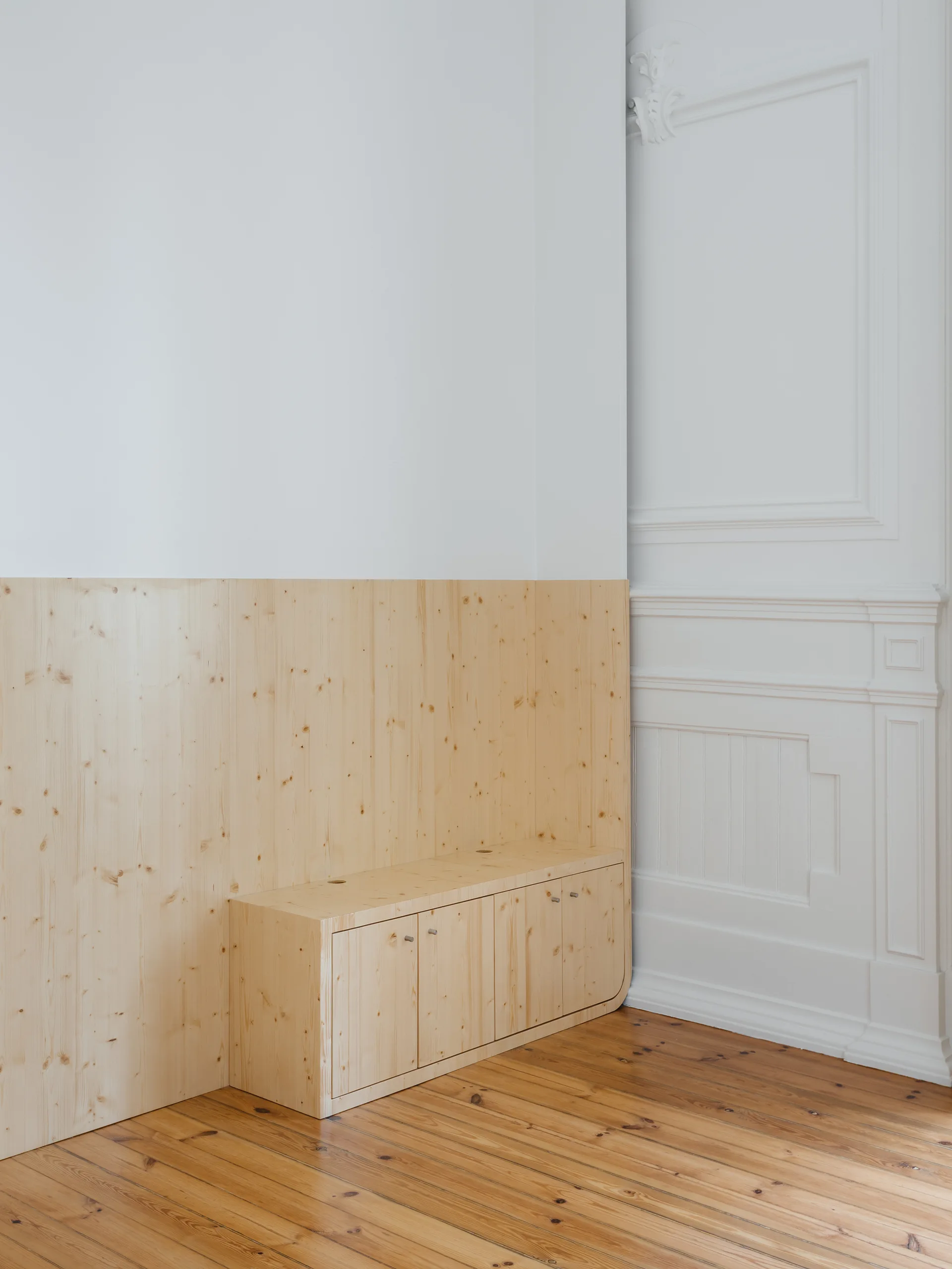 A room corner features a low light pine cabinet built into a matching wooden wall panel adjacent to decorative classical white wall molding.