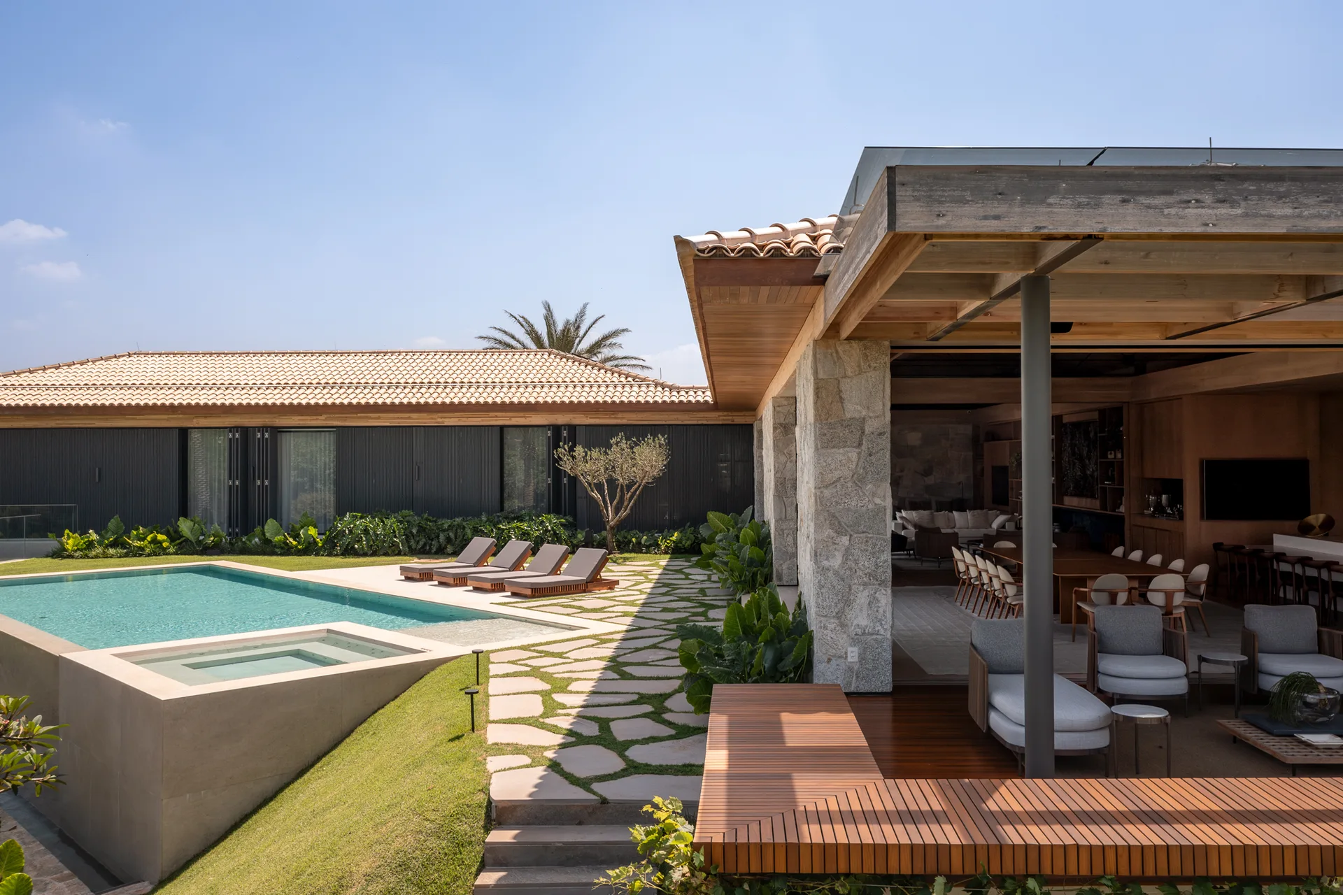A modern backyard features a blue swimming pool, lounge chairs on irregular stone pavers, and an open-sided pavilion with wood ceilings.