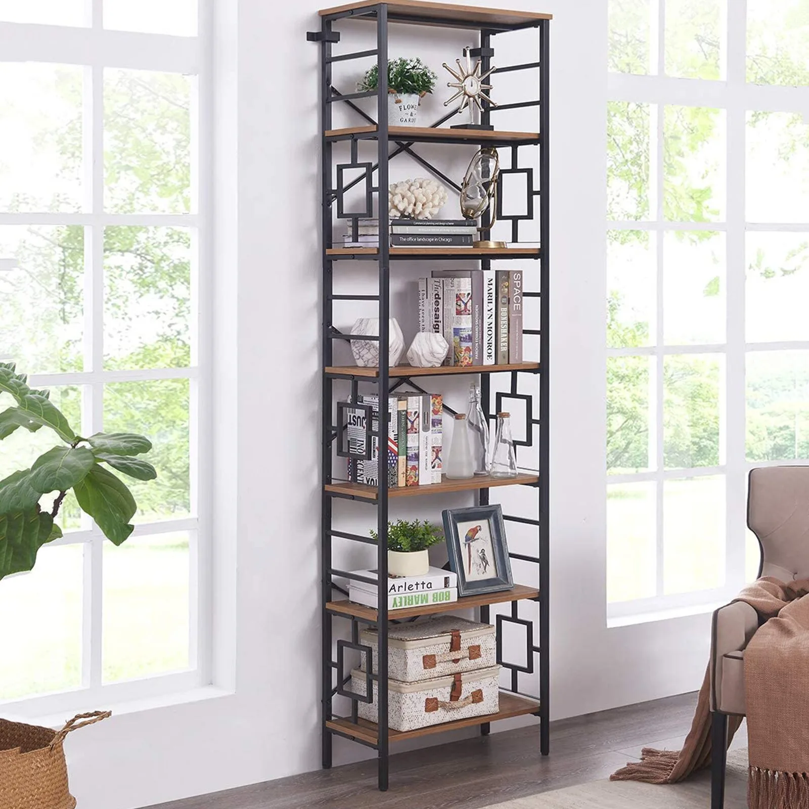 A tall black metal and wood bookshelf stands between two bright windows, displaying books, decorative items, and storage boxes.