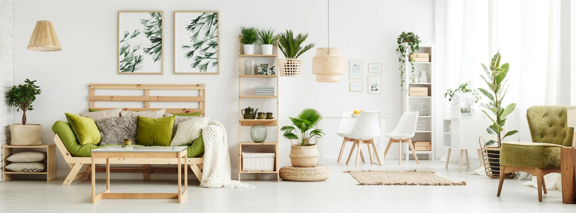 A bright living room features a wooden frame sofa with olive green cushions, botanical wall art, a tall wooden shelving unit, and potted houseplants.